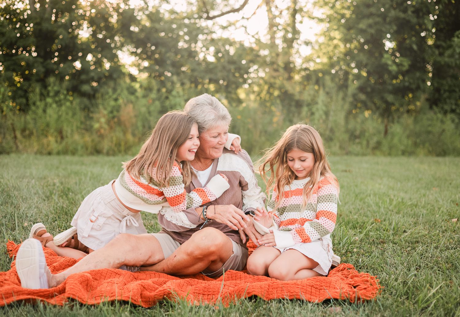 two granddaughters laughing with grandma while sitting on a orange blanket in Noblesville, IN