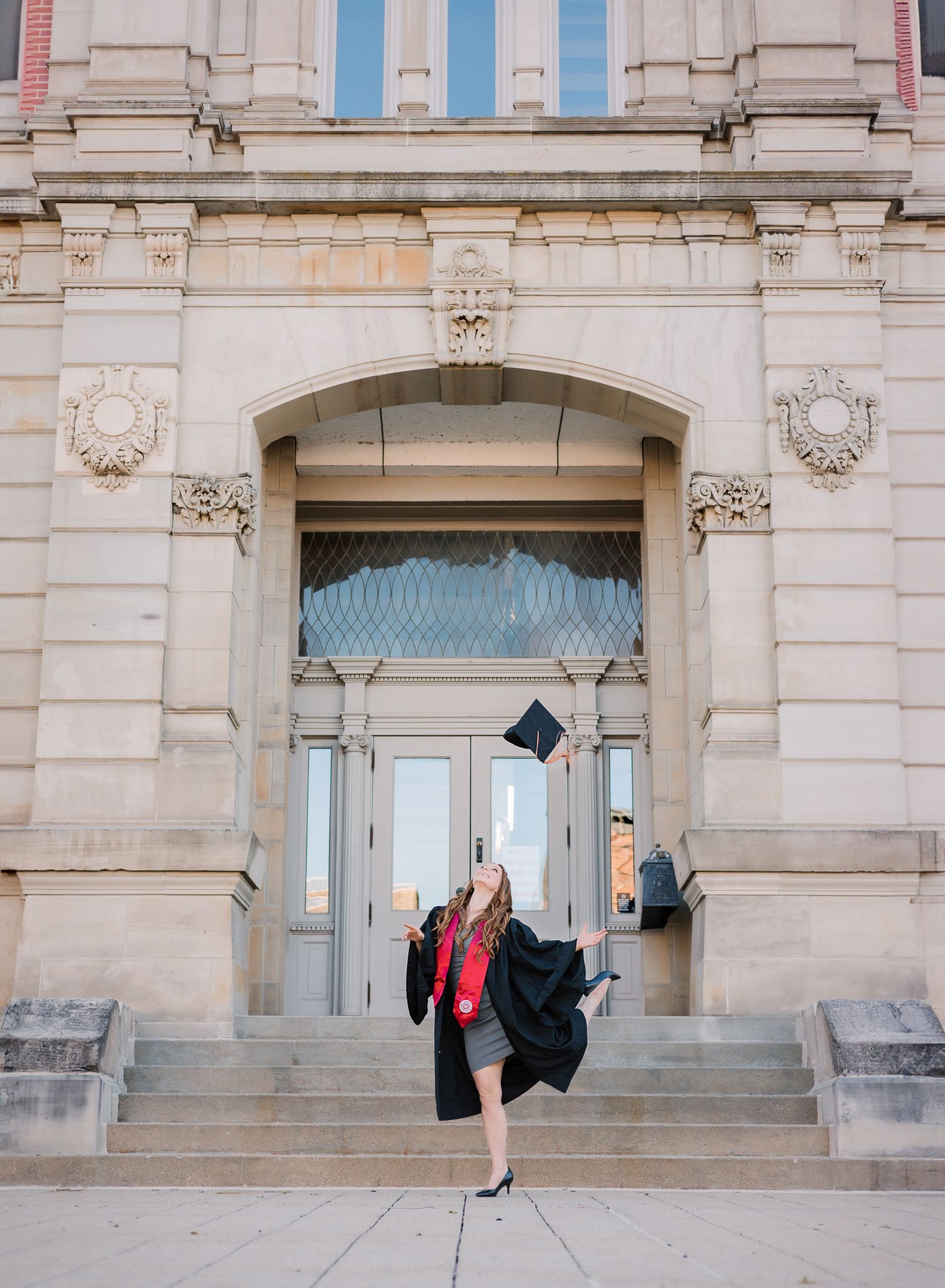 college graduate tossing up her cap in front of a courthouse in Noblesville, IN