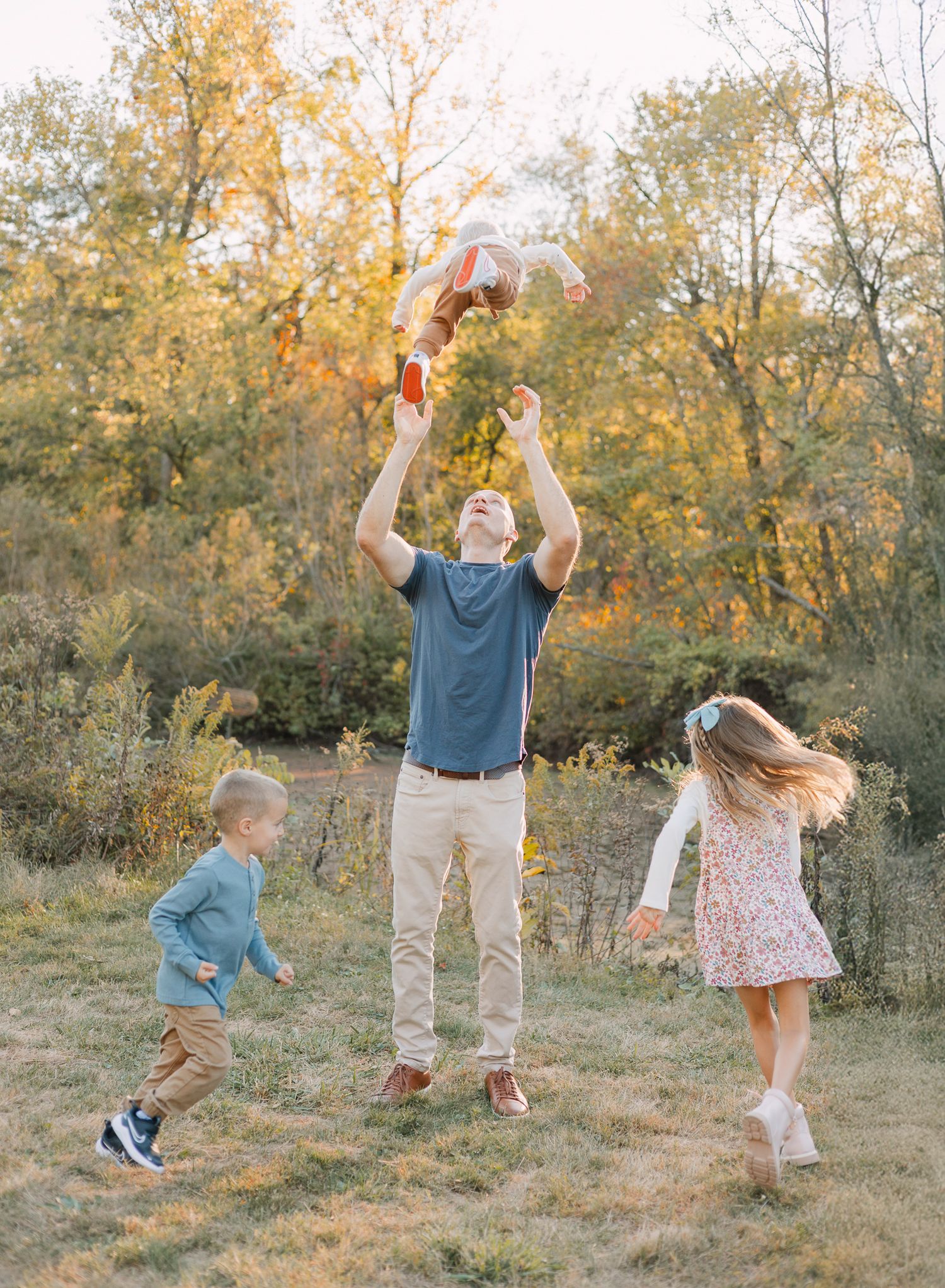 dad tossing baby in air with two siblings running around in Fishers, IN