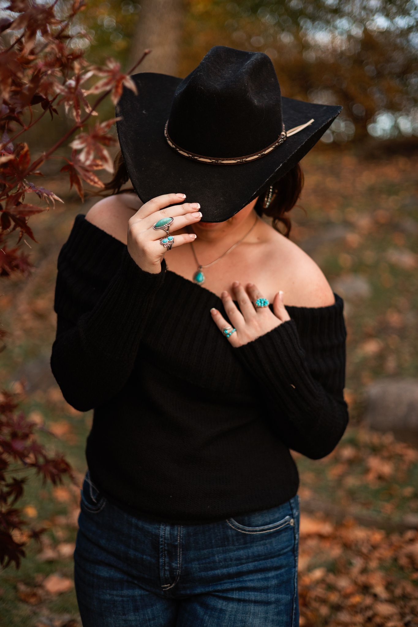 senior girl wearing a black sweater and jeans with her hand on her sweater and the other tipping her hat in Pendleton, IN