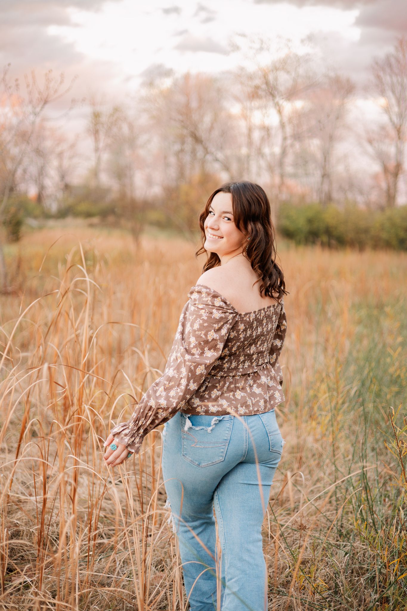 senior girl looking back at the camera while walking through a field in the fall in Pendleton, IN