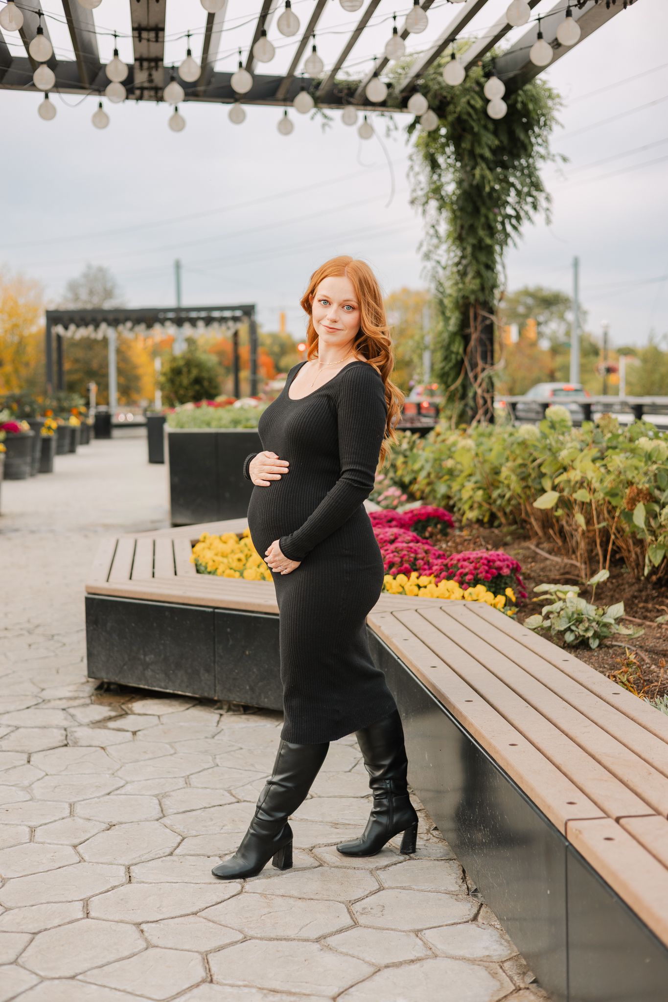 maternity session in Noblesville woman in black dress under pergola with hands on baby bump