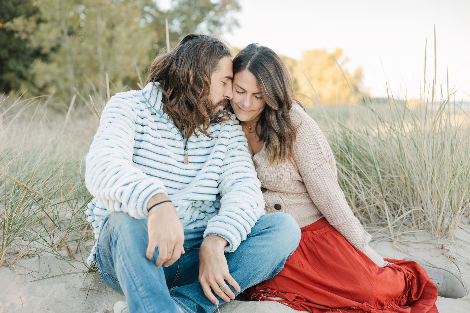 wife in rust colored dress leaning into husband sitting at the dunes