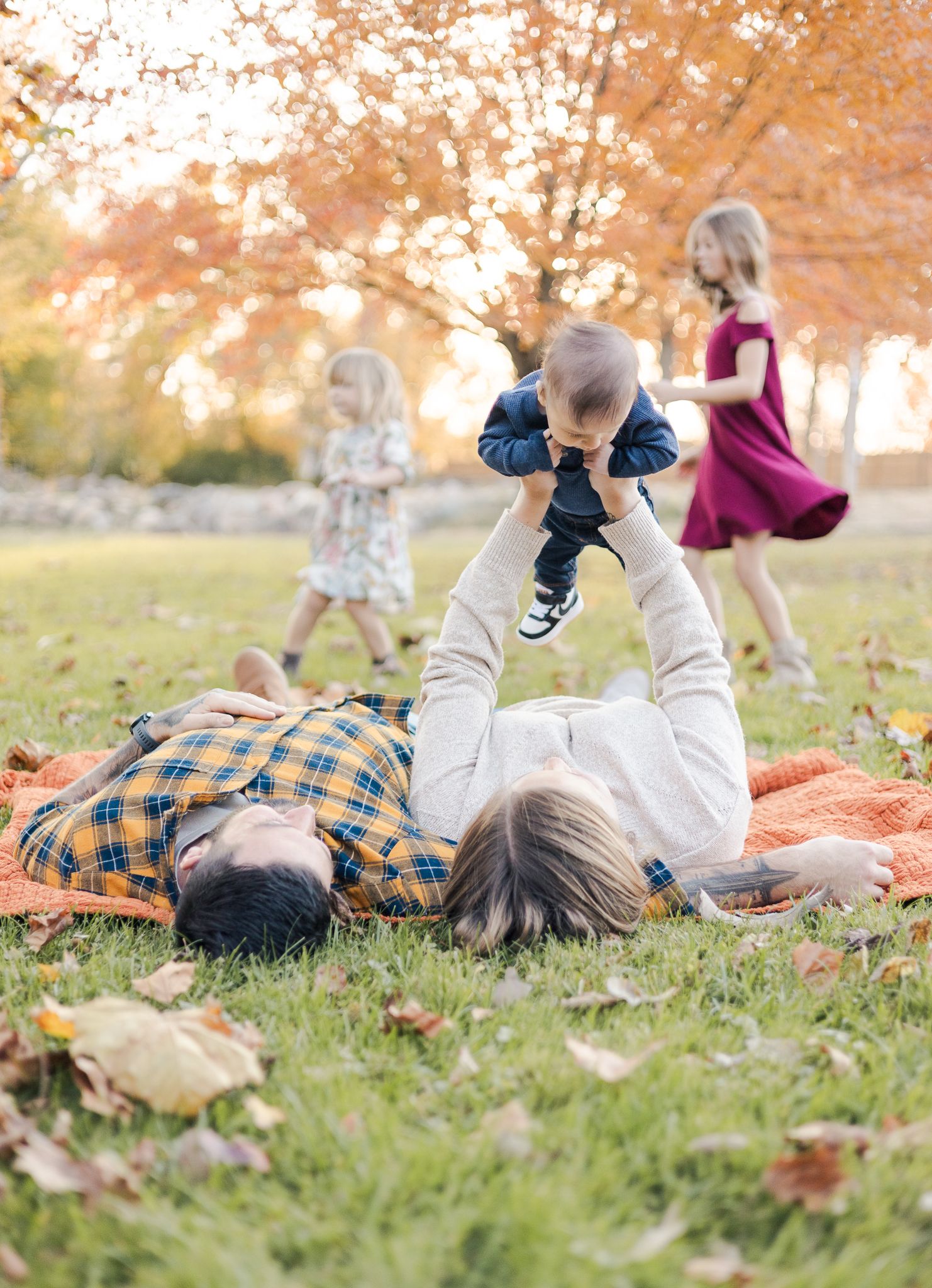 mother holding baby while laying on ground next to husband while the child run around in the background in Pendleton, IN