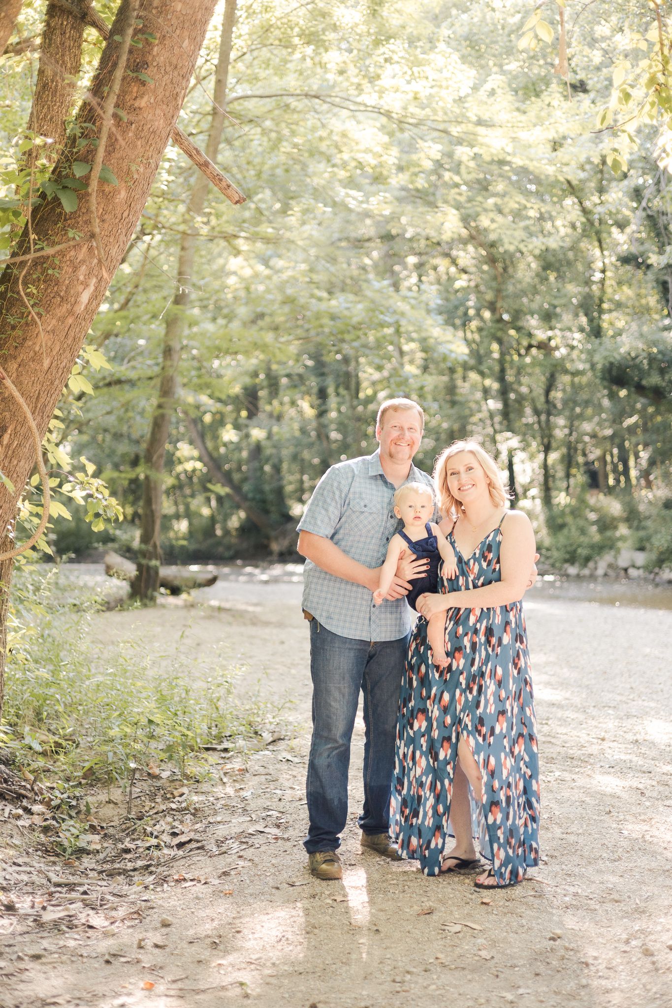 mother and father standing under a tree with son by the creek