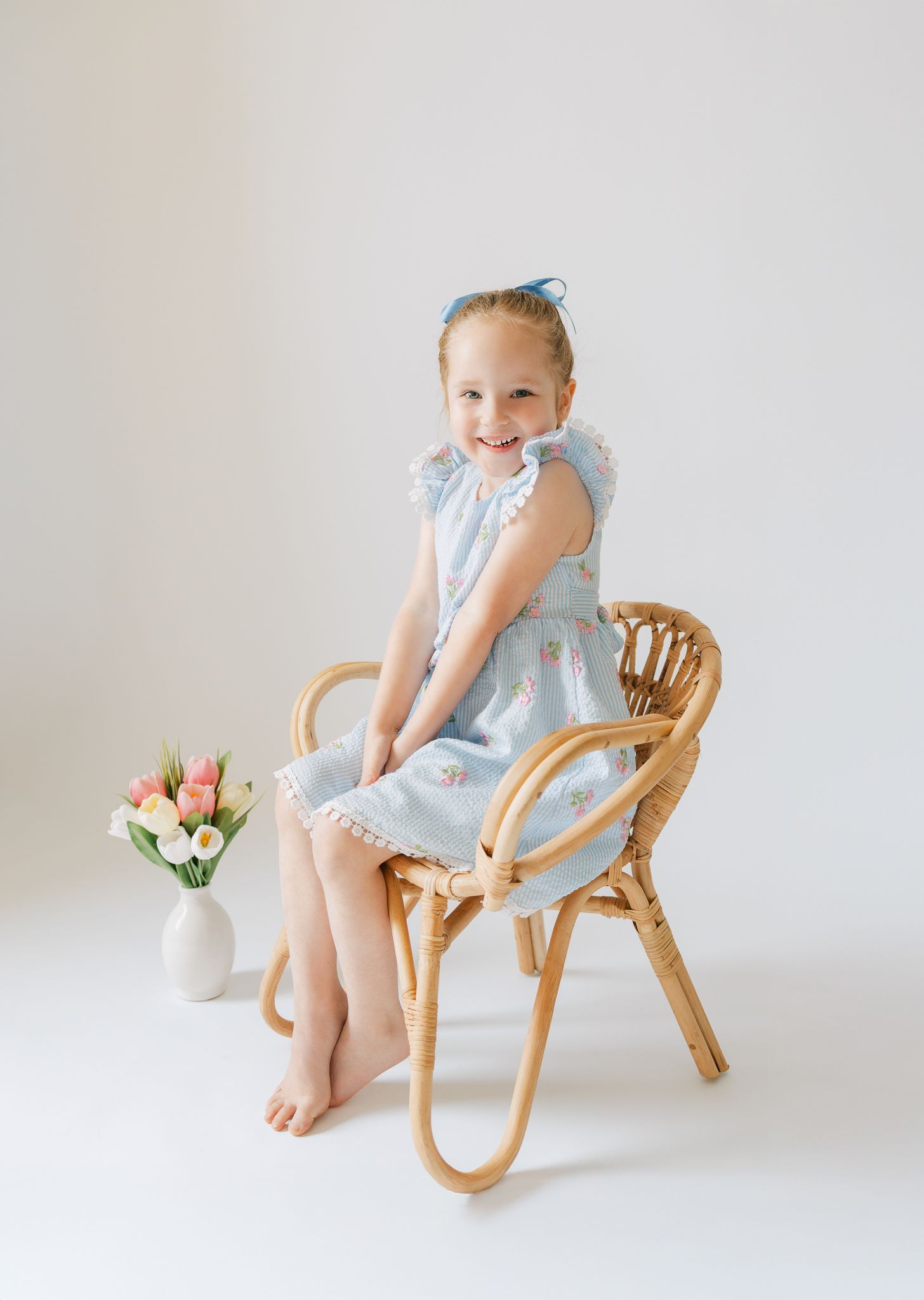 little girl in wicker chair with tulips in vase