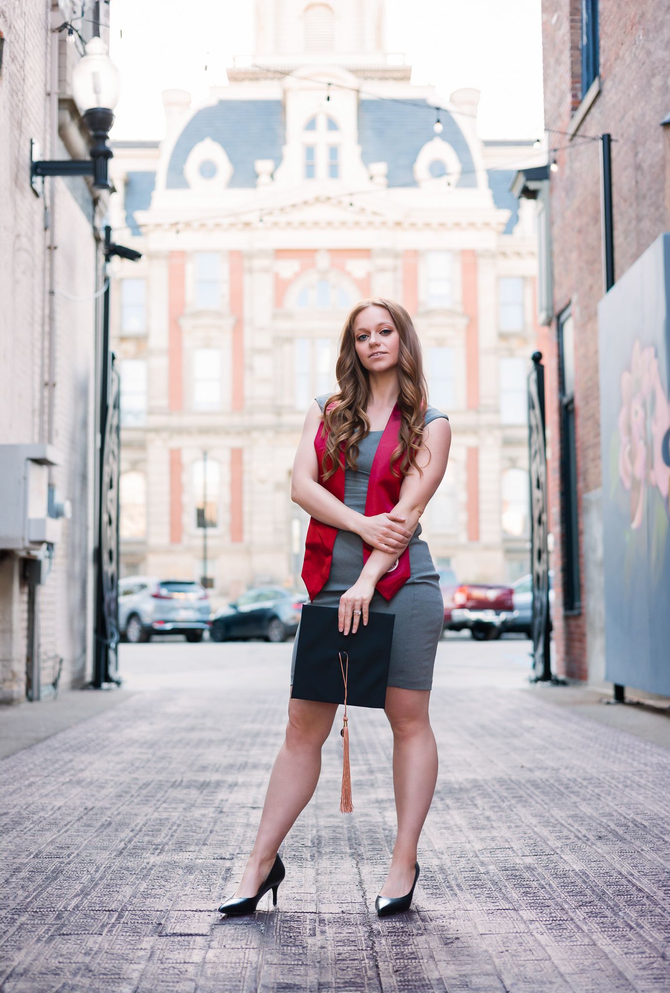 college graduate standing in a brightly lit alley while holding her cap in Noblesville, IN