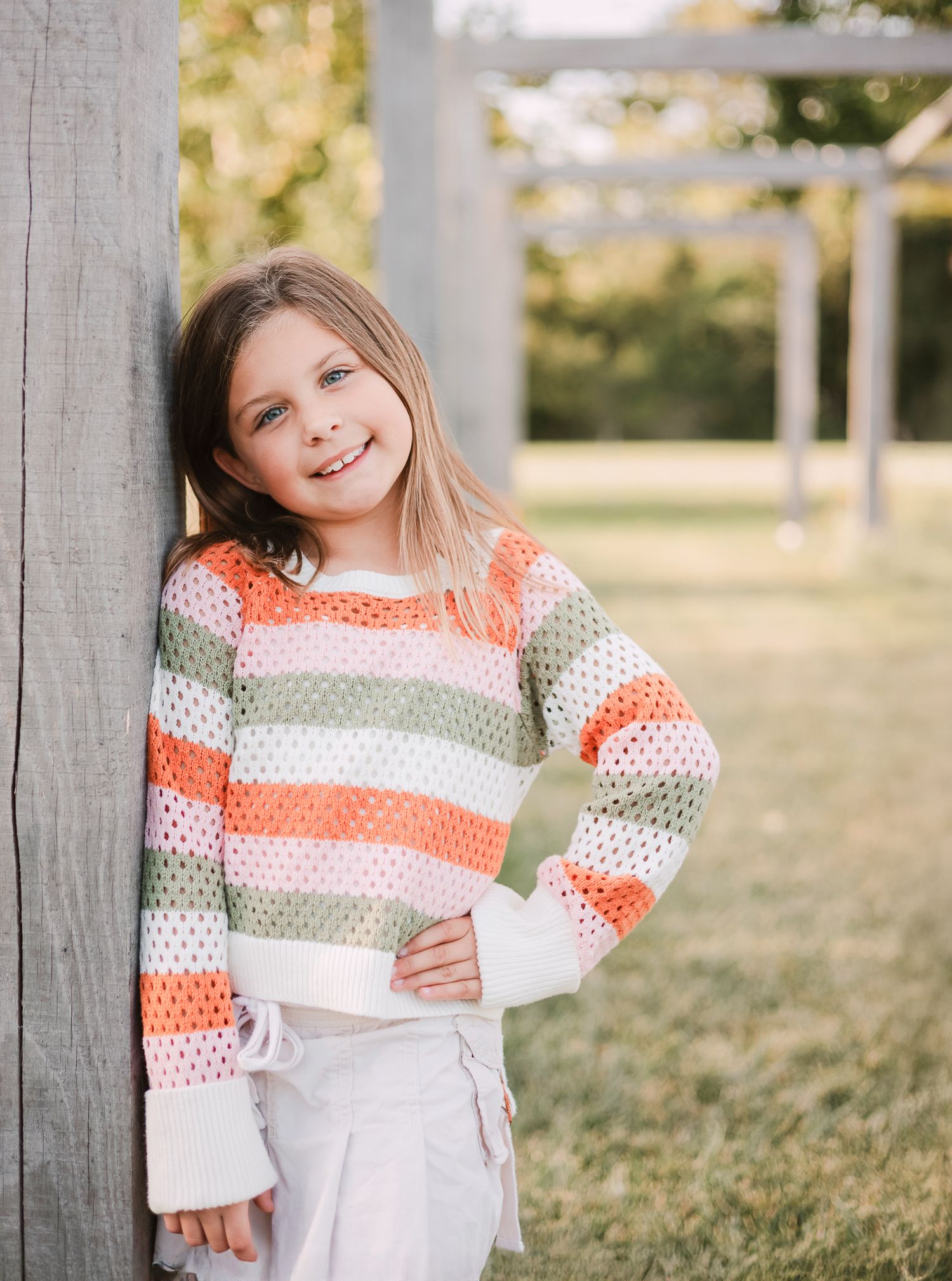 child leaning against a post with her hand on her hip
