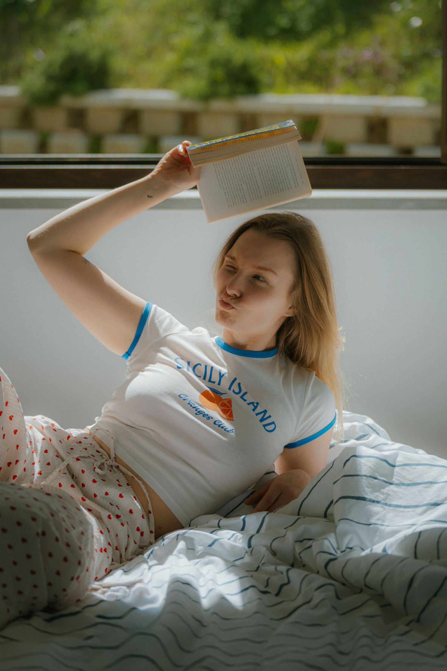 Relaxed reading moment in bed with soft natural lighting from nearby window.