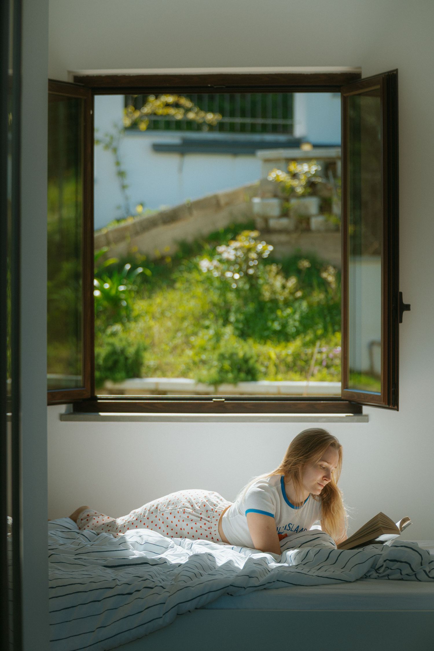 Cozy bedroom scene with natural light flowing through an open window overlooking a garden.