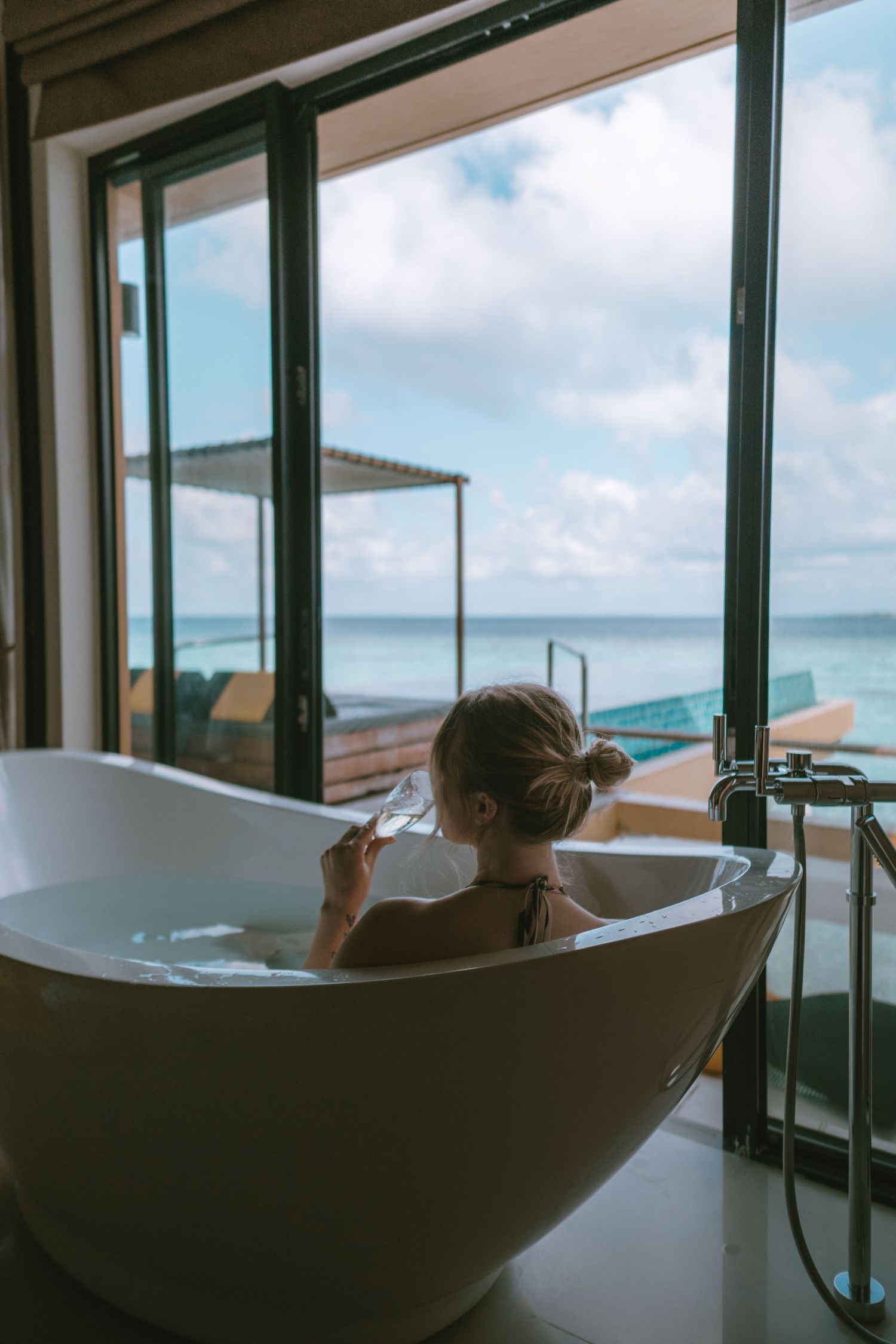 Luxurious freestanding bathtub with panoramic ocean views through floor-to-ceiling windows.