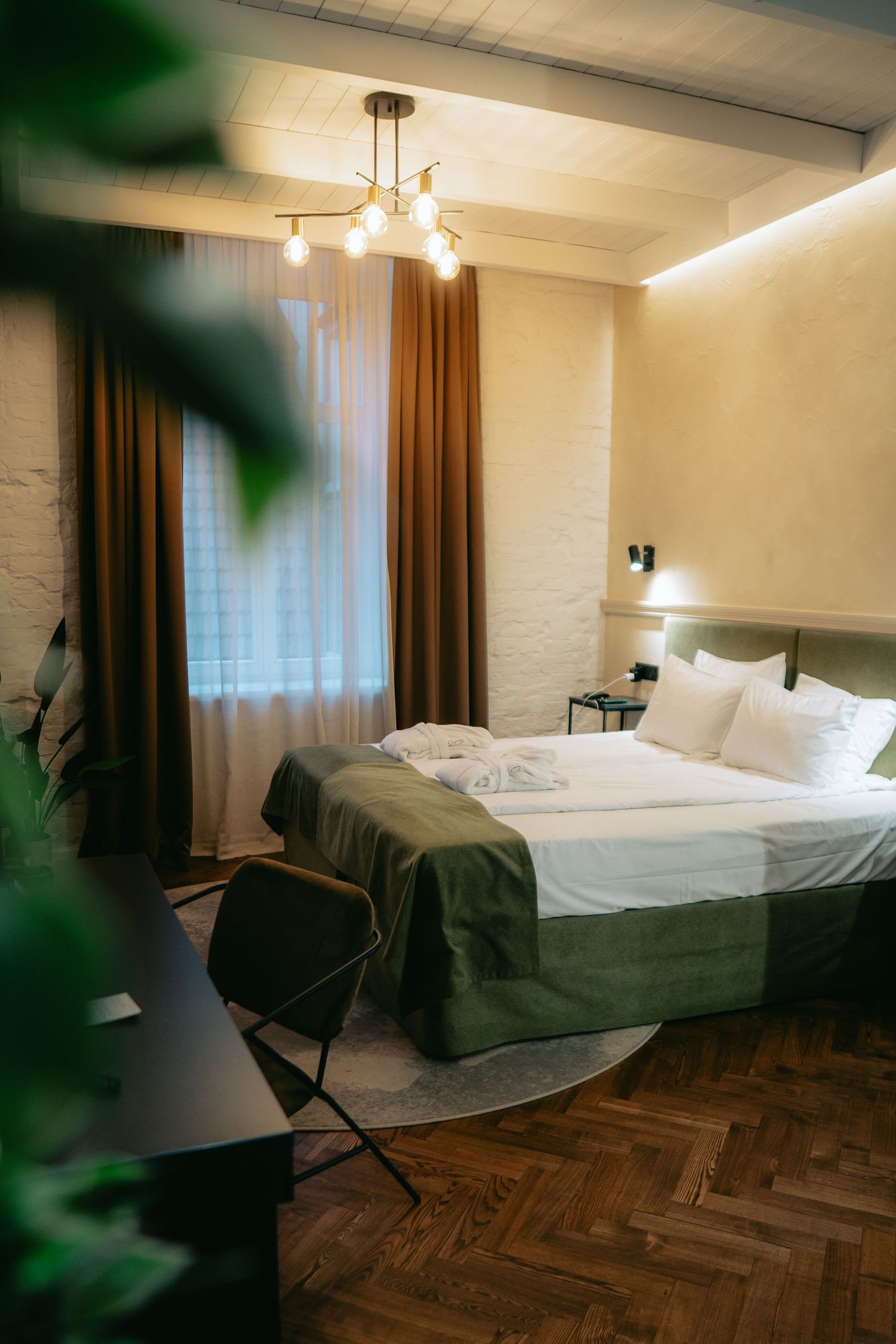 Modern hotel room interior with white beds, wooden floors, and brown curtains.