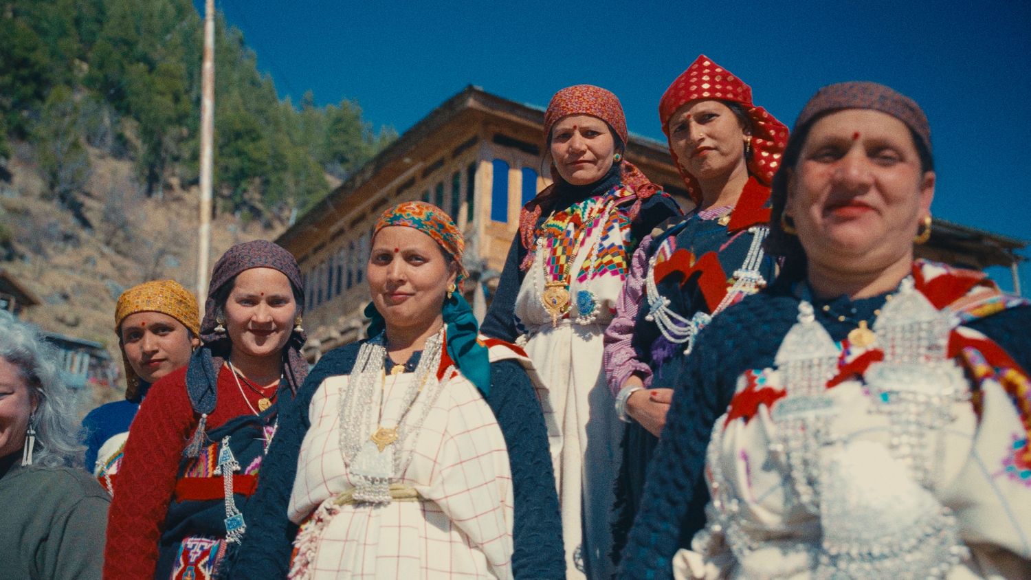 Group of women in traditional folk costumes and colorful headscarves gathered outdoors at a cultural festival.