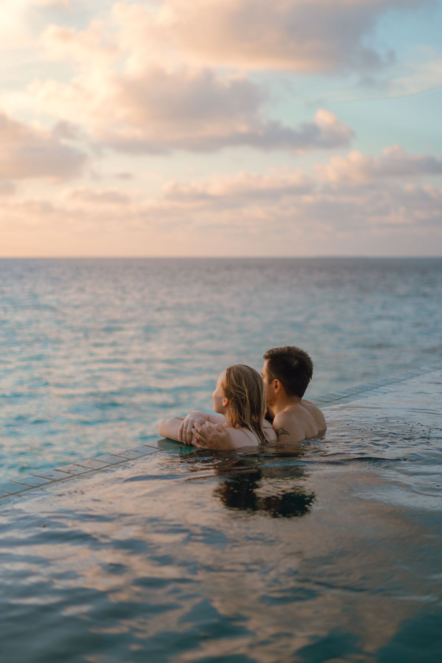 Couple floating in crystal clear ocean waters during a romantic sunset moment.
