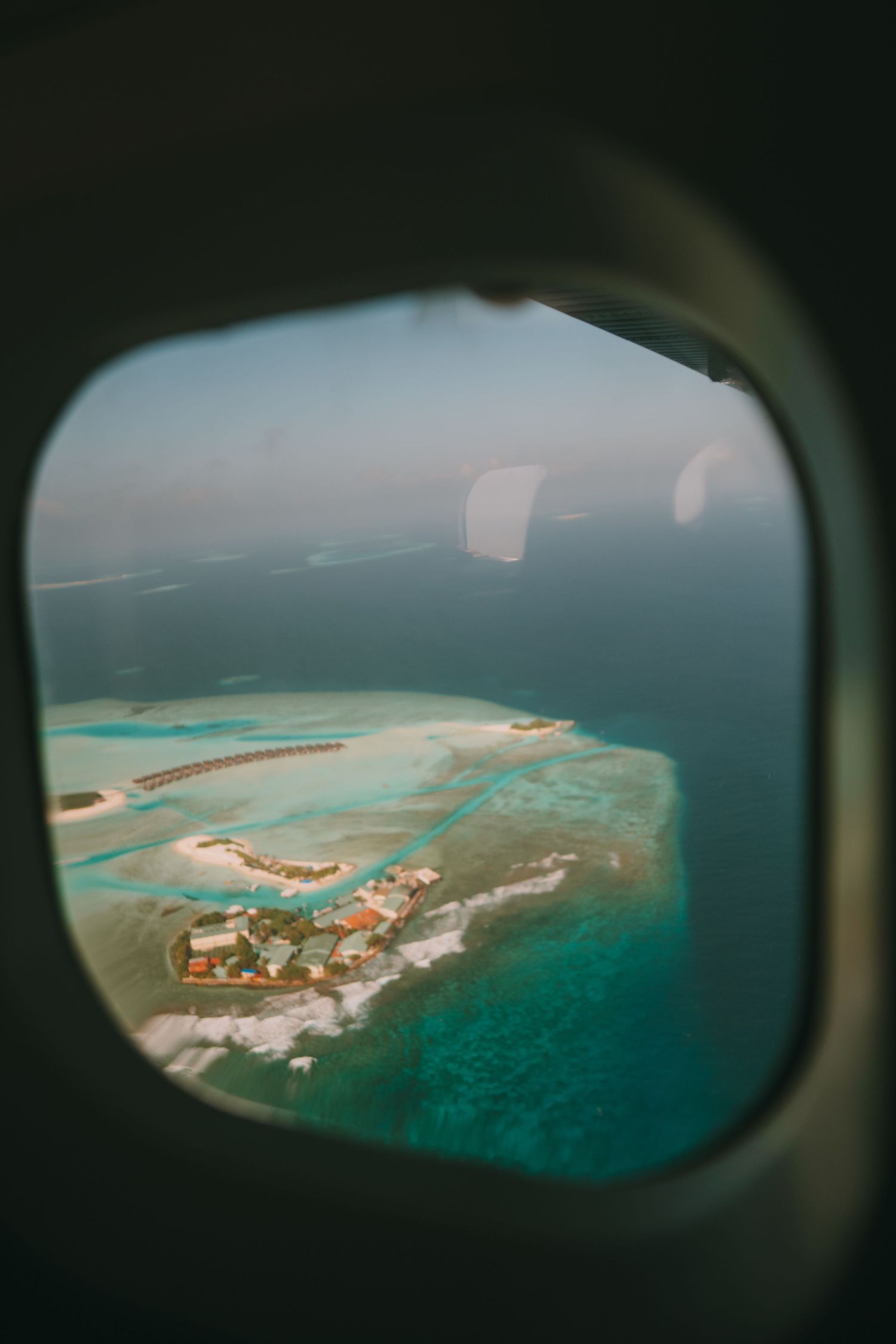 Aerial view of a tropical island resort through an airplane window showing turquoise lagoons.