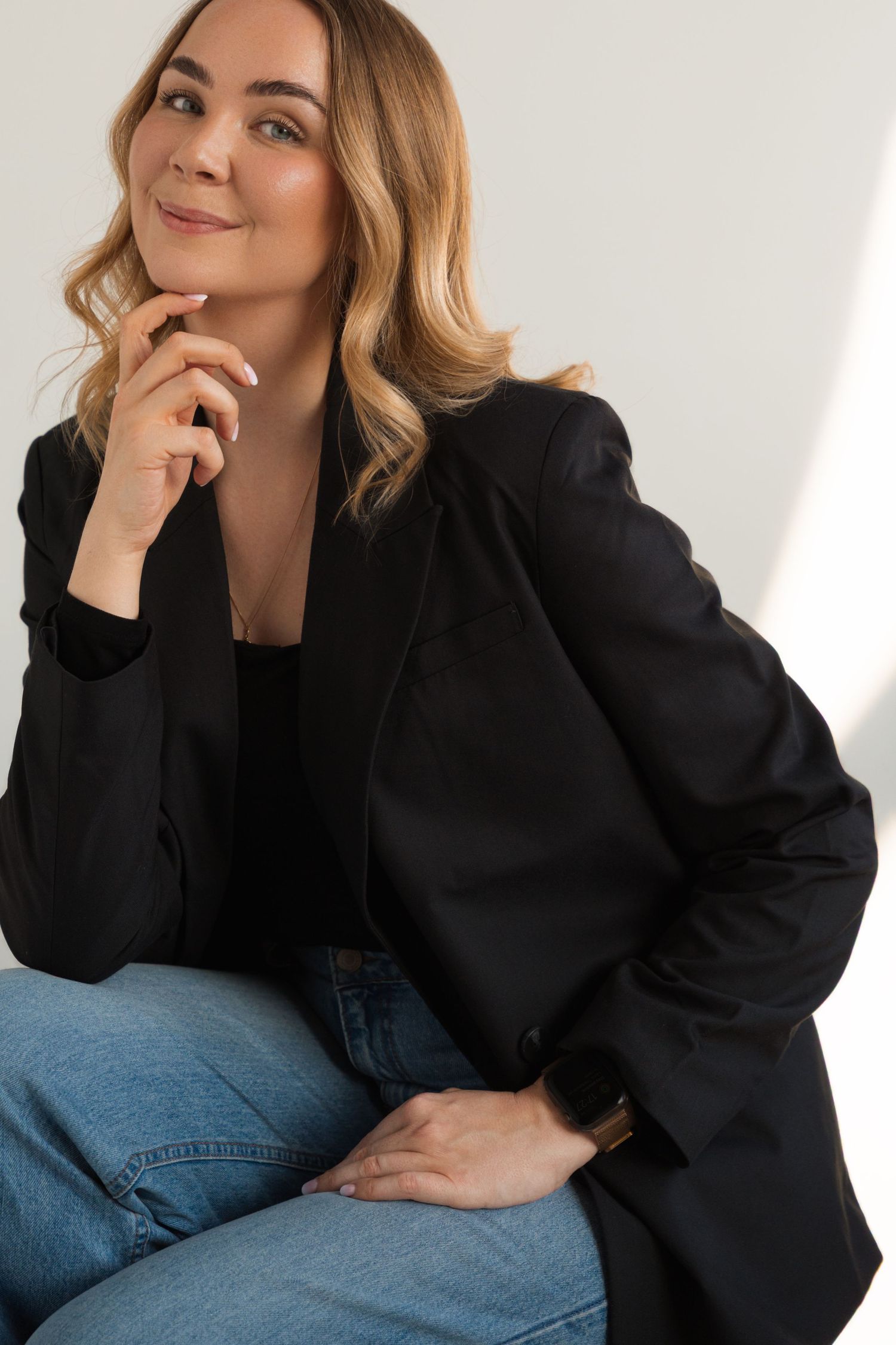 Professional portrait in black blazer and jeans against white background.
