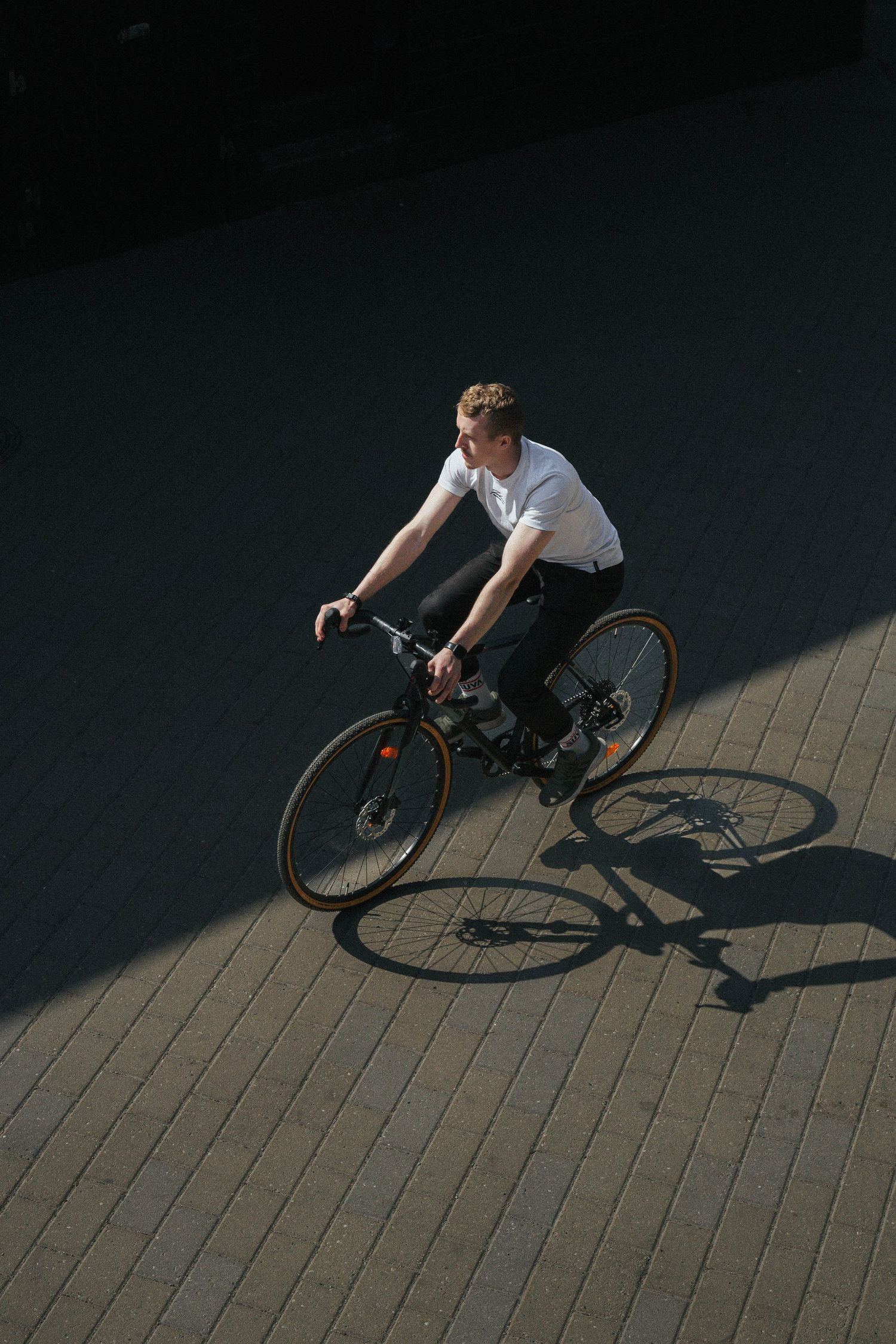 Dramatic aerial view of a cyclist riding on textured pavement in harsh sunlight and shadow.