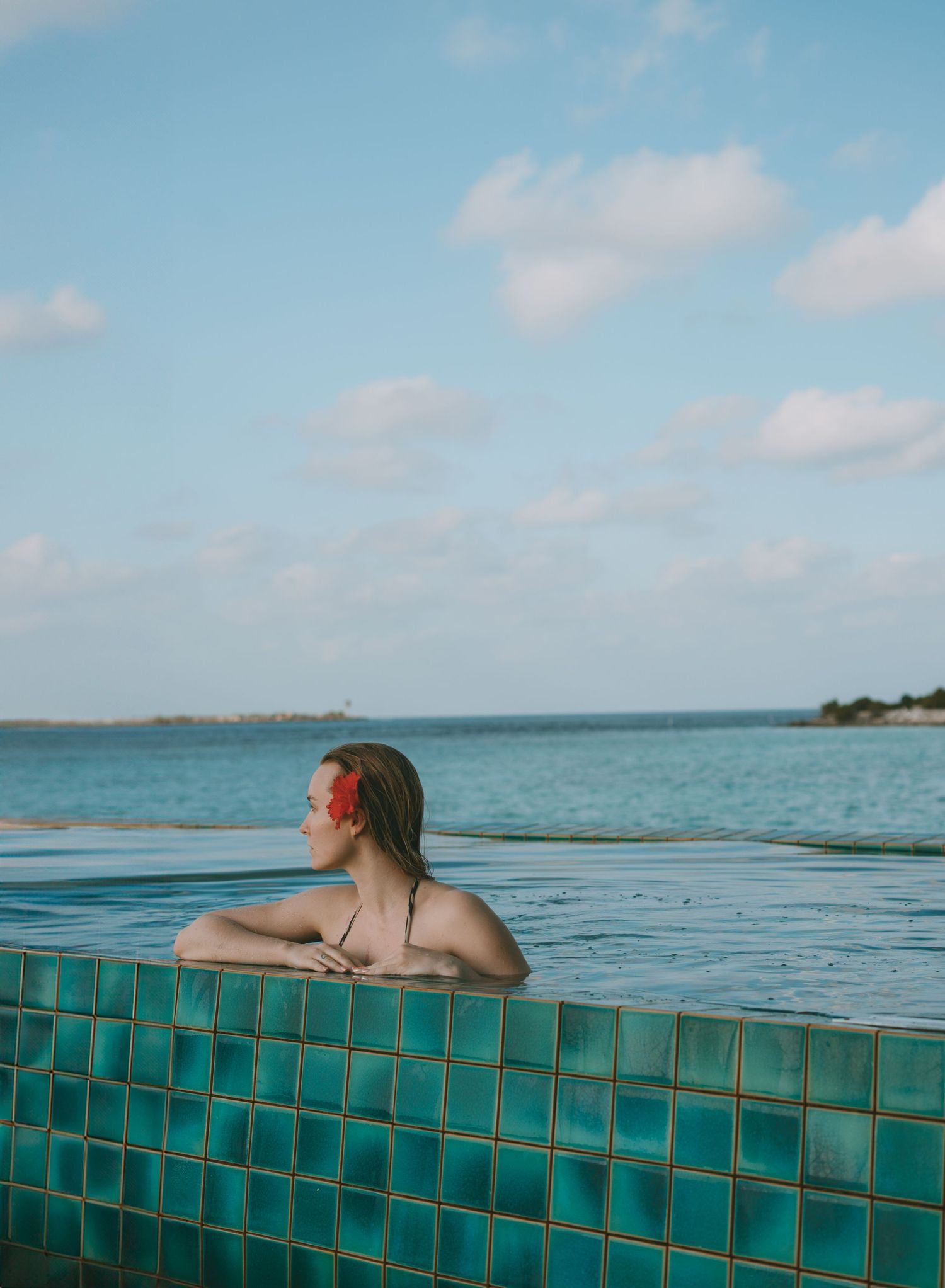 Turquoise infinity pool overlooking a calm ocean horizon on a bright sunny day.