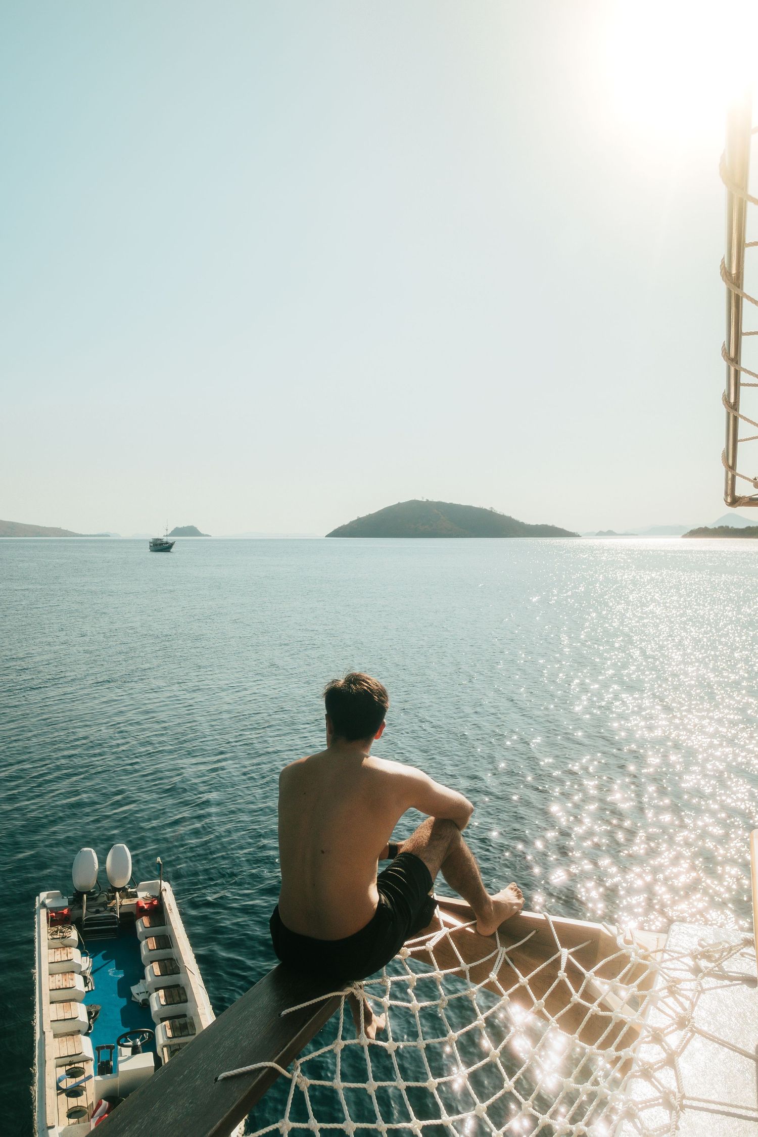 Passengers relaxing on sailboat deck netting while cruising through sparkling ocean waters.