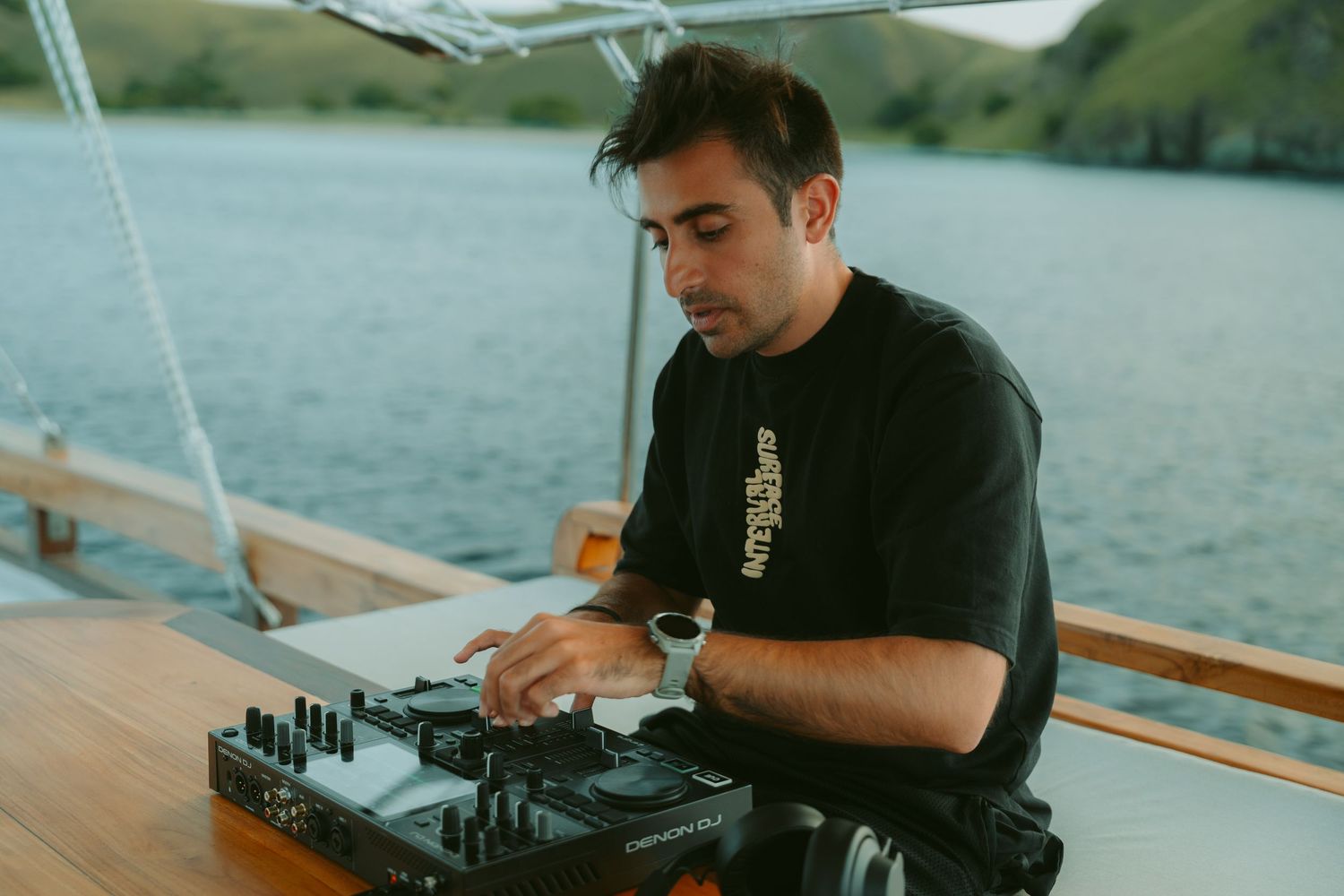 DJ mixing music on professional equipment at an outdoor waterfront venue during sunset.