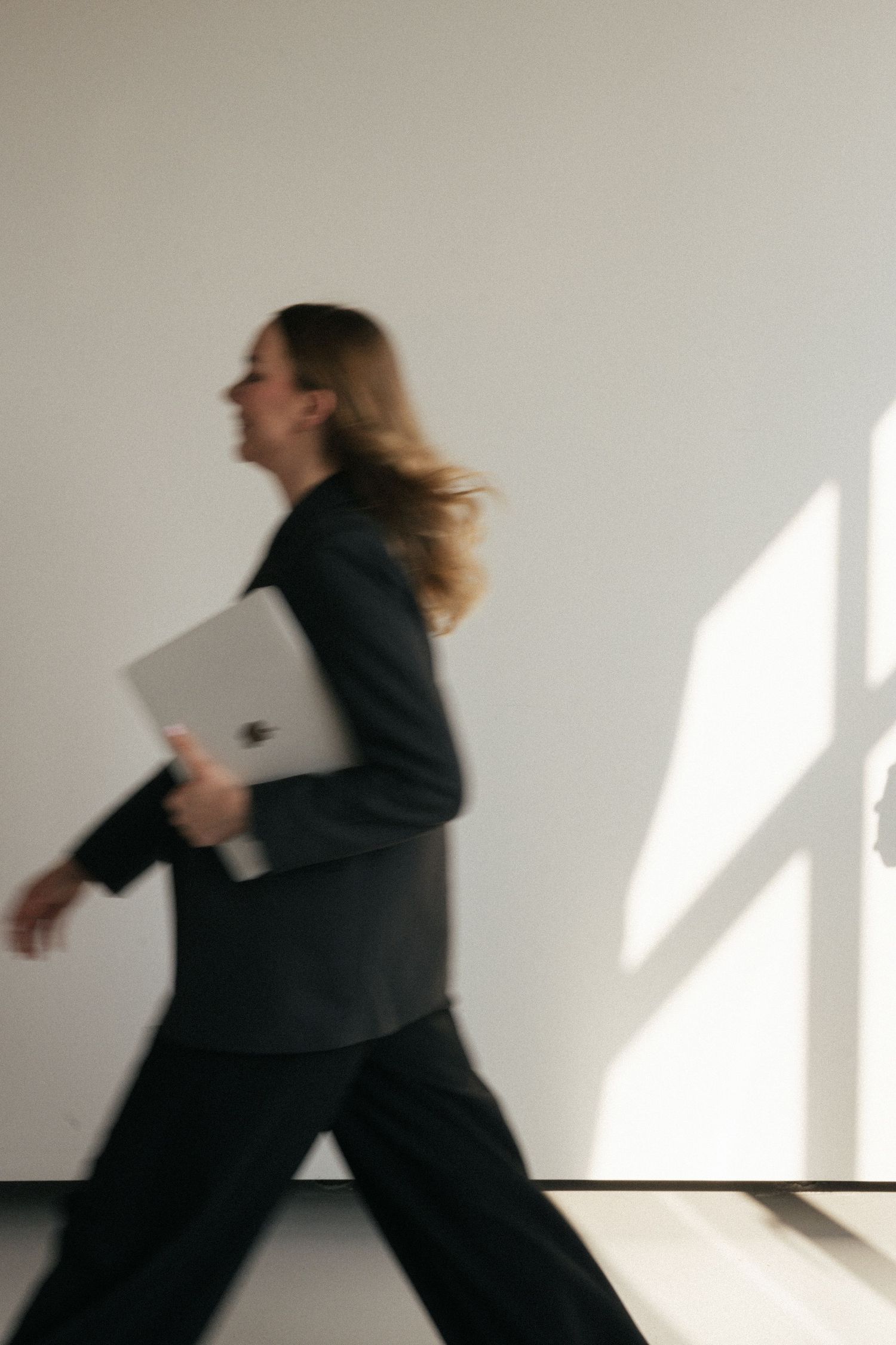 Motion blur sequence of person in black outfit running through sunlit white space.
