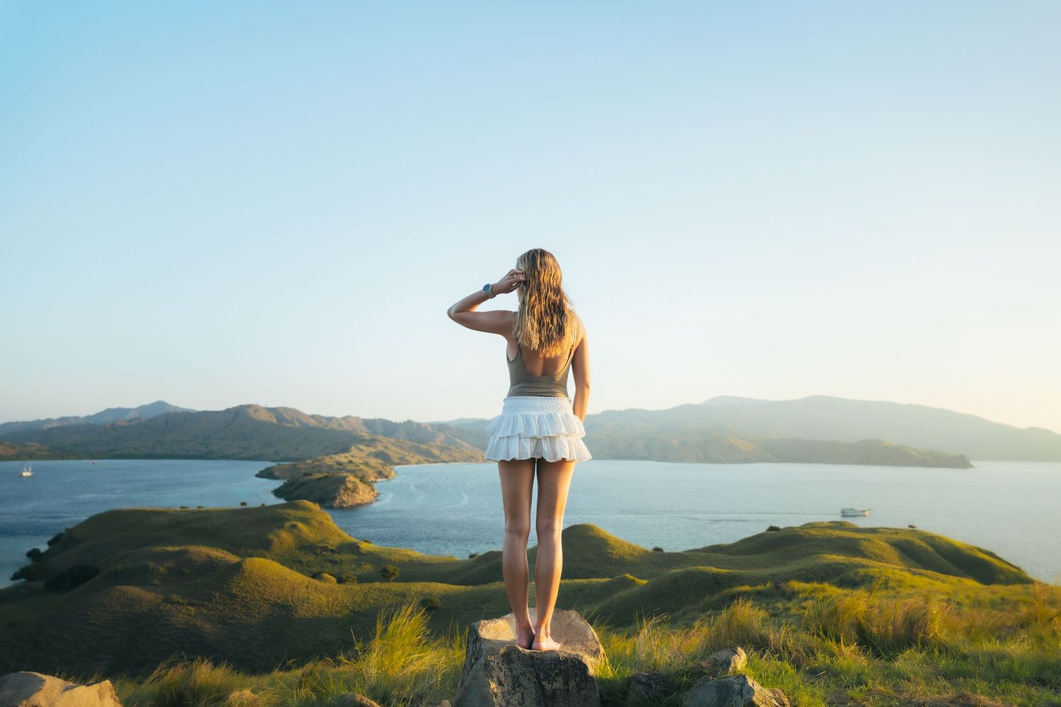 Person enjoying scenic coastal view from hilltop during golden hour.