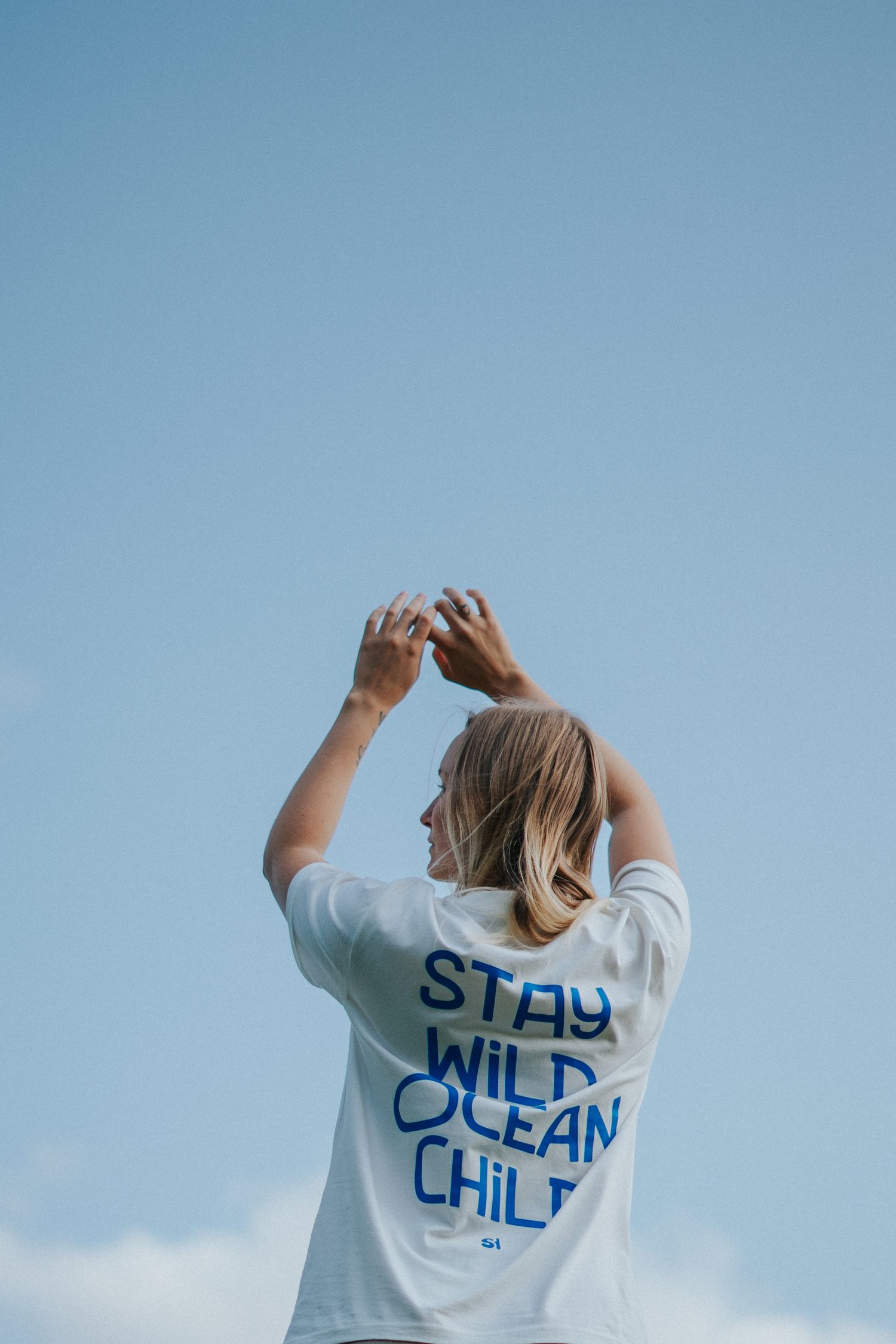 Person in white t-shirt with text 'Ocean Child' photographed against blue sky.