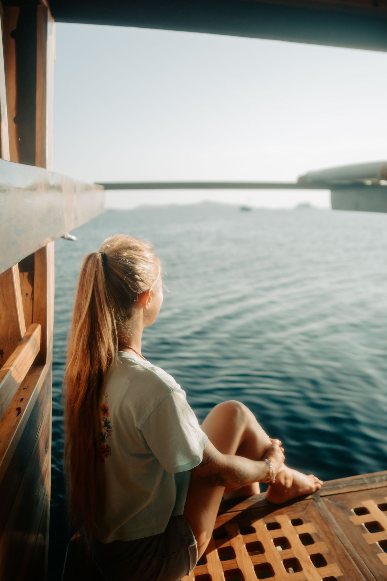 Passenger relaxing on wooden deck of boat while sailing across calm ocean waters.
