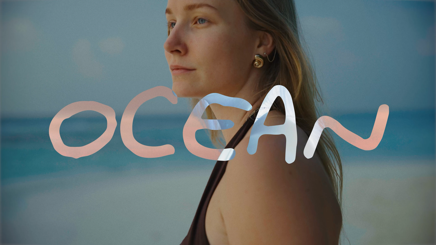 Young woman at beach with ocean backdrop, text overlay reading OCEAN in stylish gradient lettering.