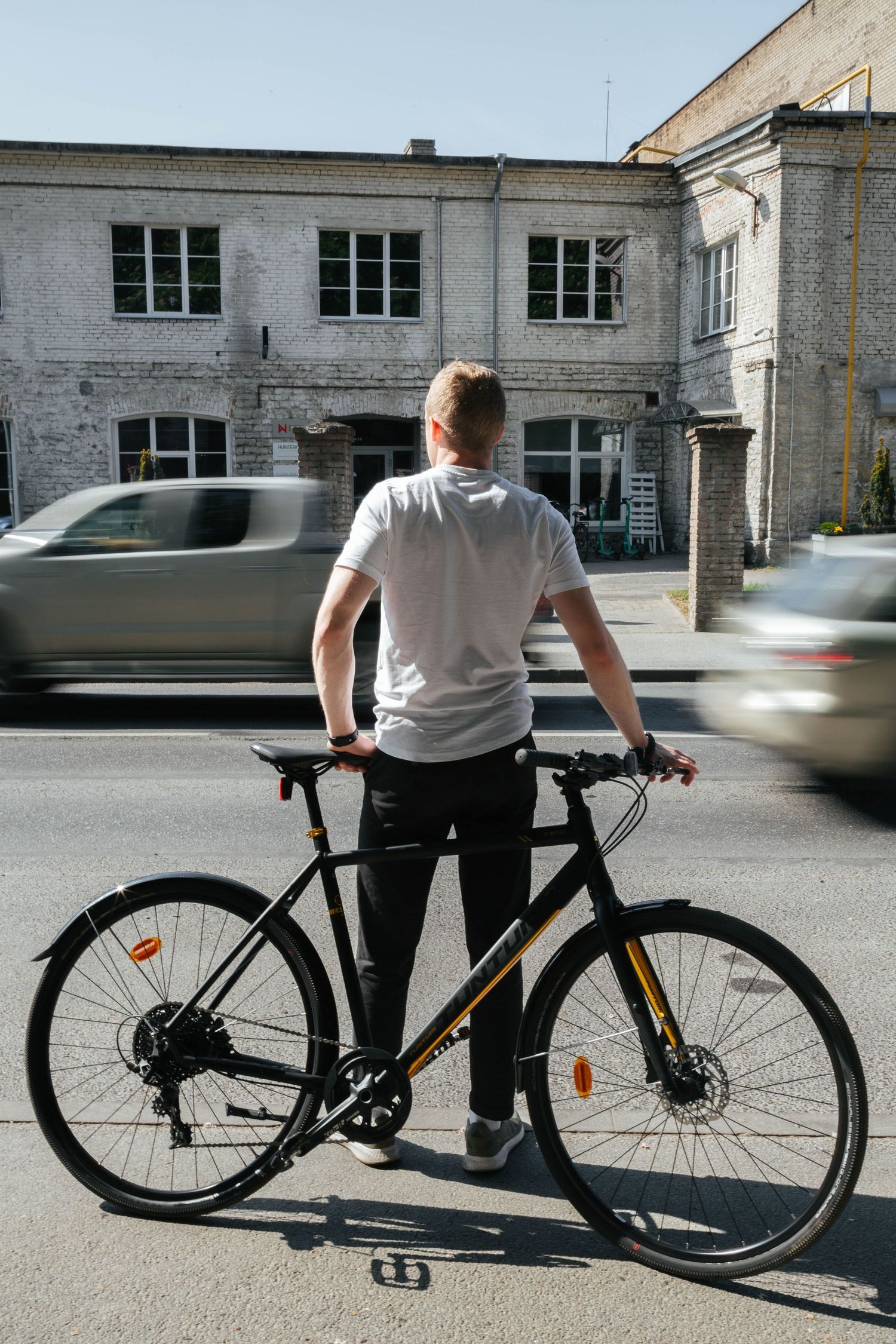 Sequential shots of cyclist with black bike against industrial building exterior.