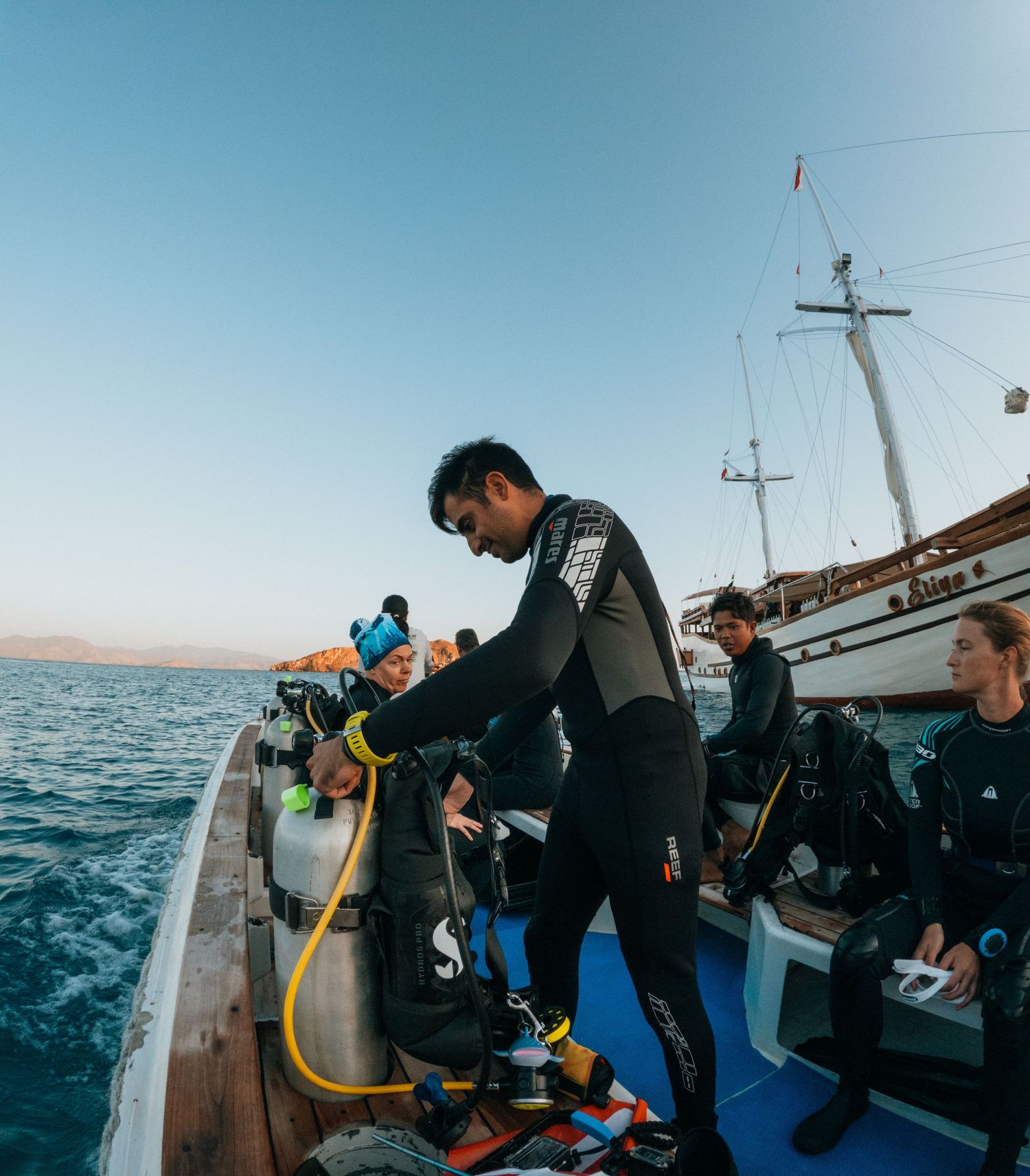 Scuba divers preparing equipment on a boat deck against blue ocean backdrop.