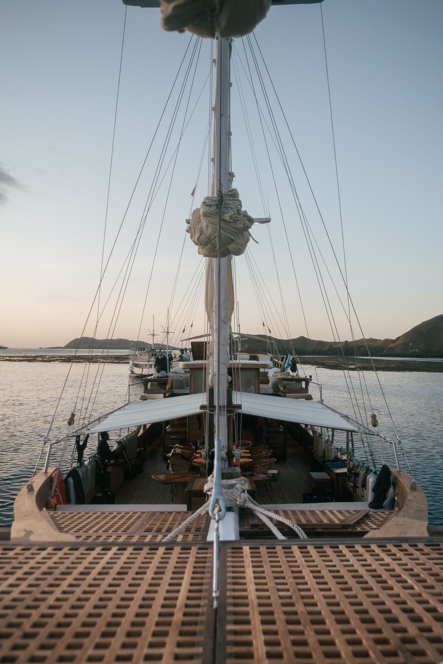 View of a wooden sailboat deck with rigging and masts against a clear blue sky.