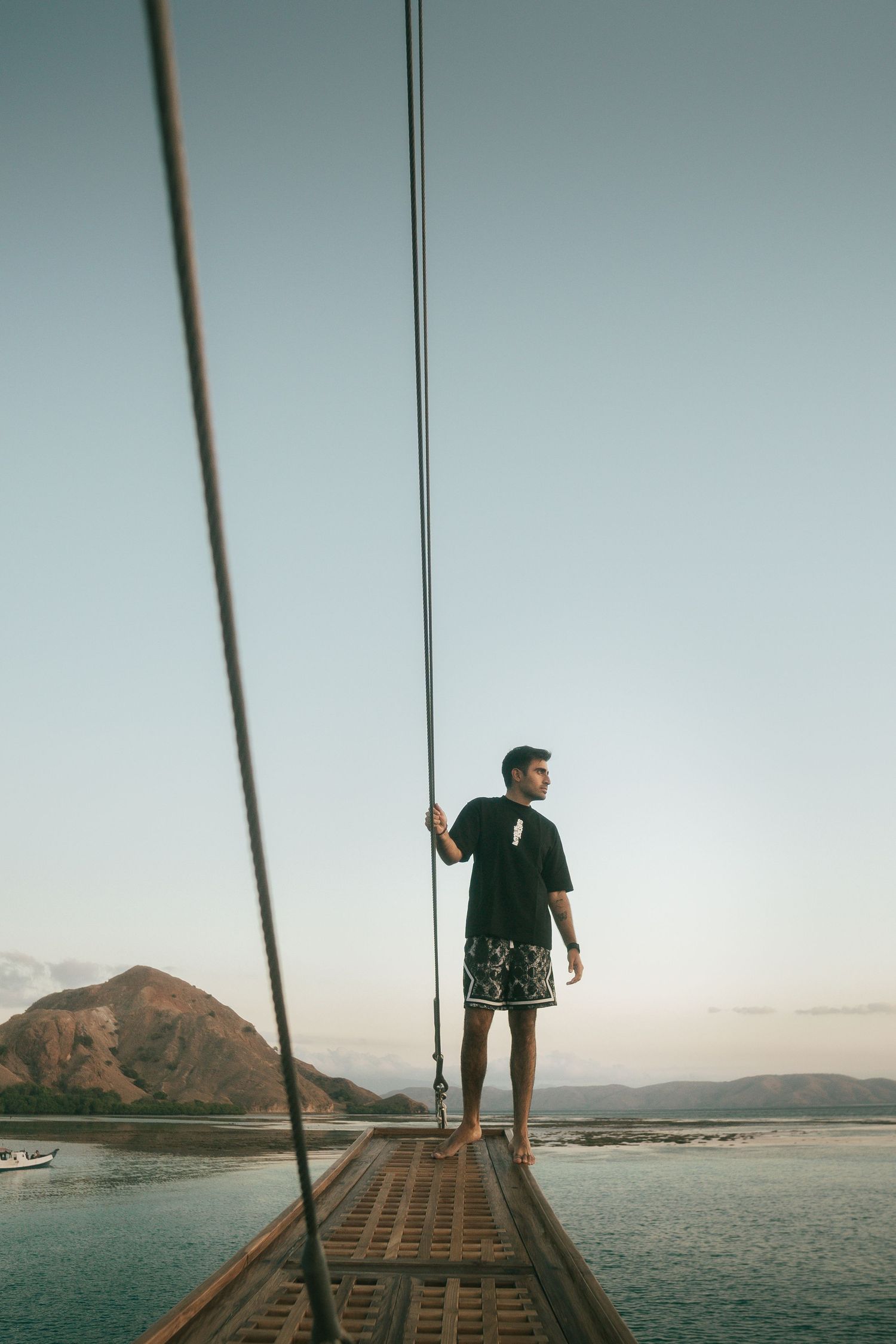 Person stands on wooden pier overlooking mountainous coastal landscape at sunset.