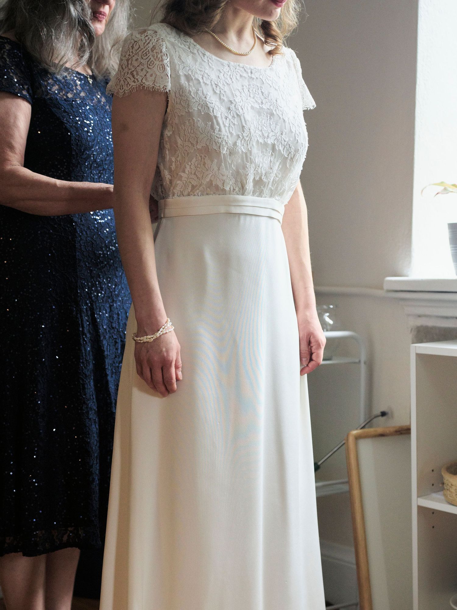 Detail shot of white lace wedding dress with navy blue dress in background.