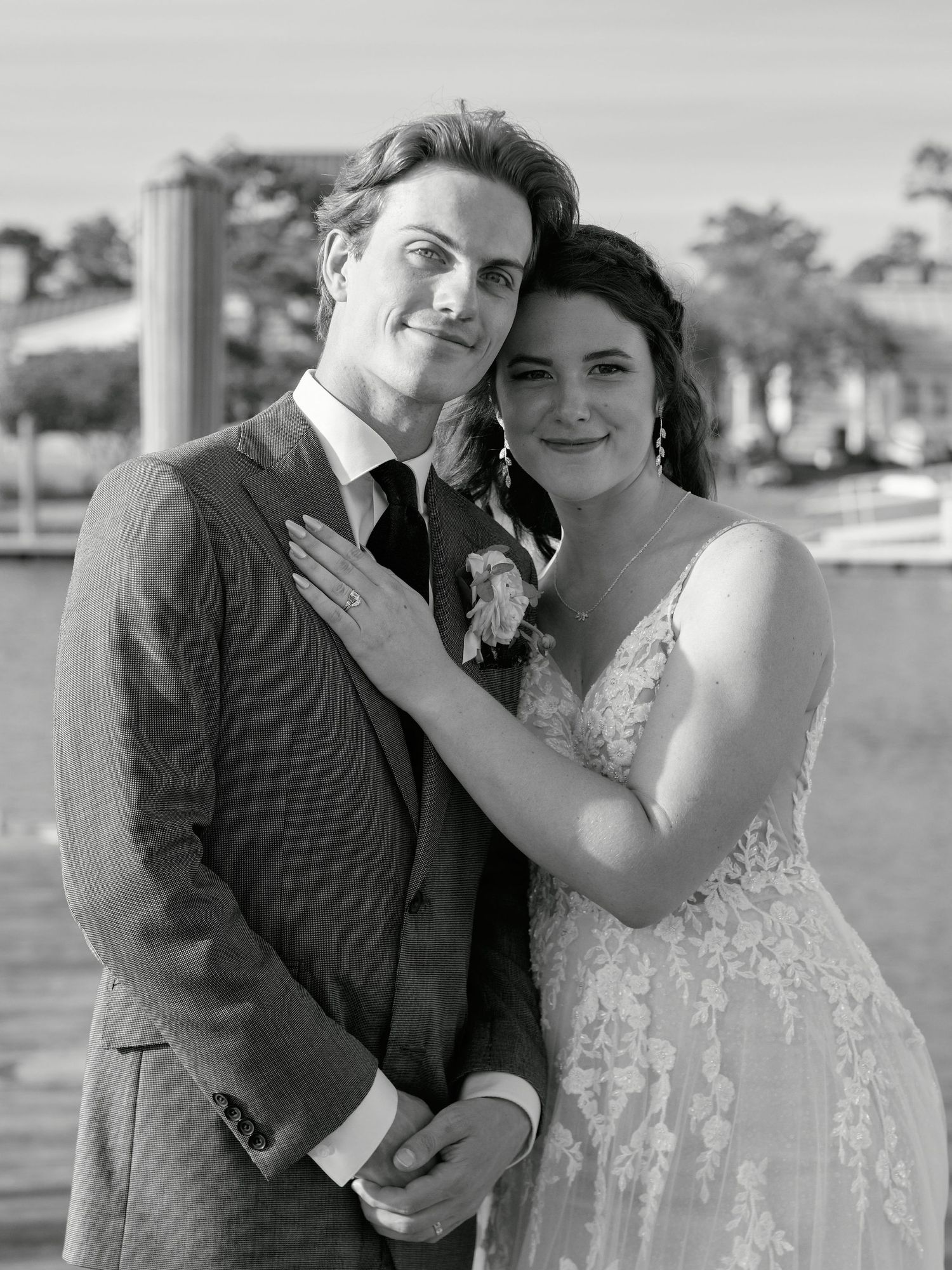 A black and white wedding photo of a couple outdoors with the bride in a lace dress and groom in a suit.
