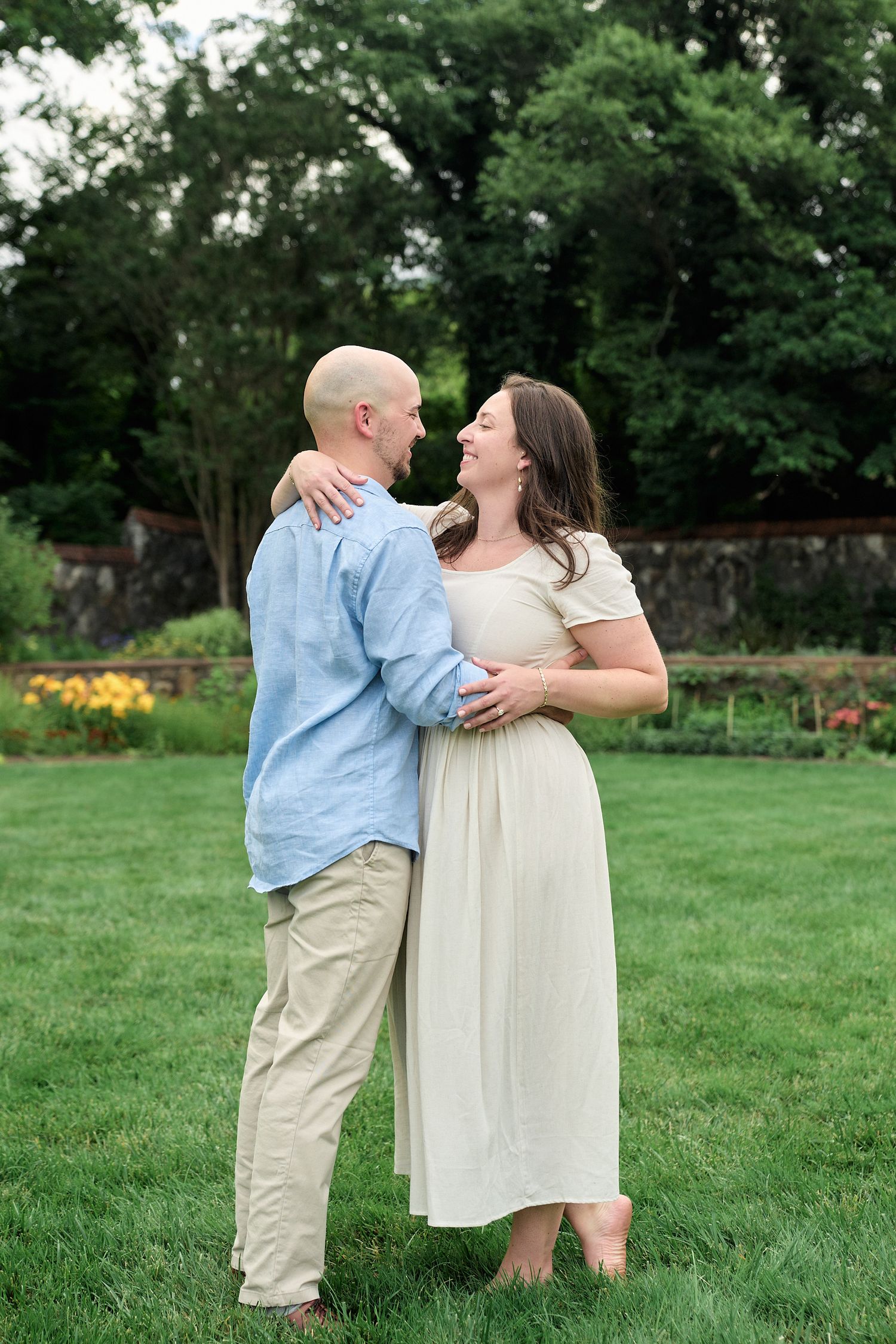 A romantic embrace captured in a garden setting with flowering plants and stone walls.