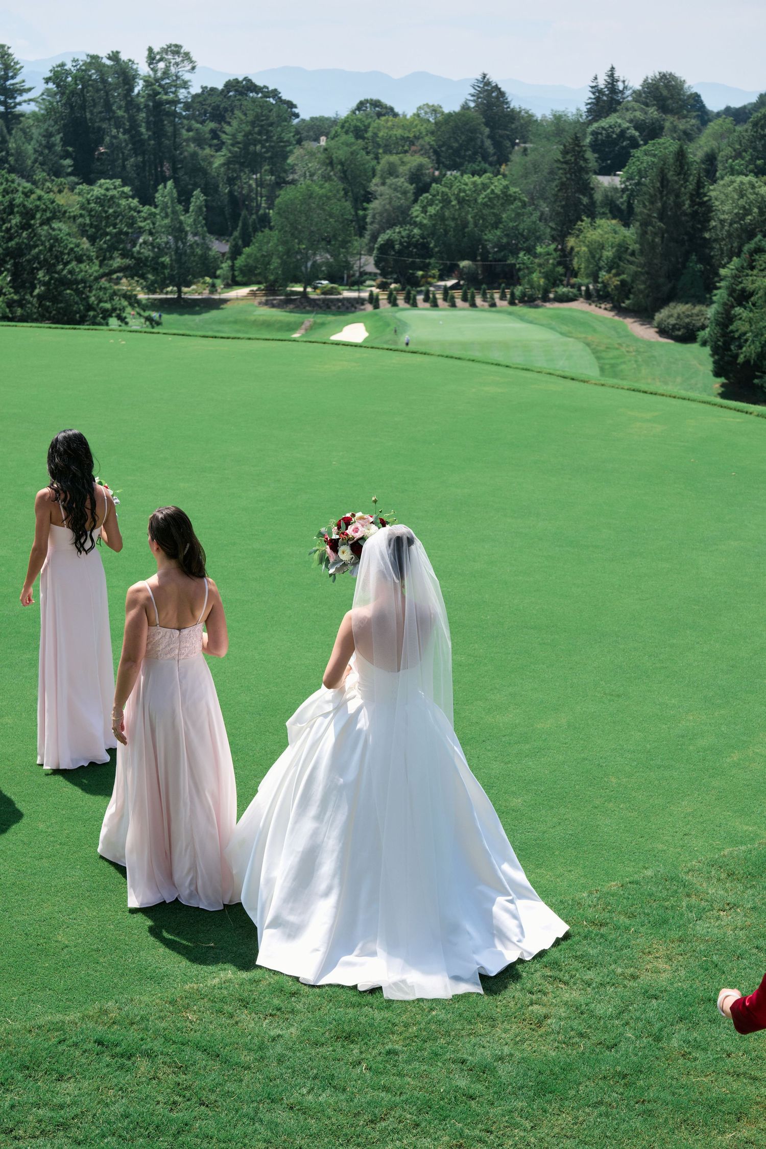 A bride and bridesmaids walk across a manicured golf course green.