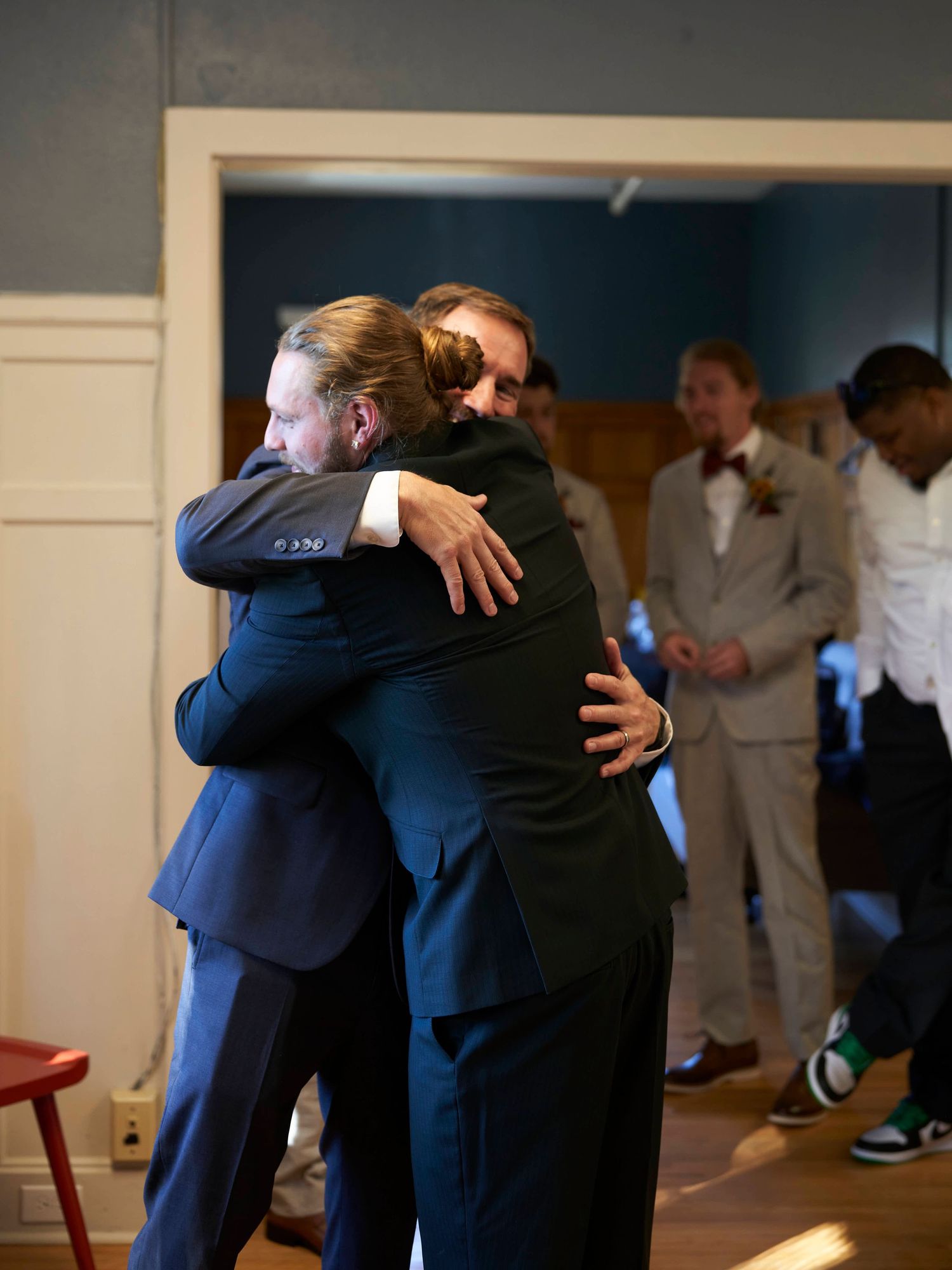 Two people sharing an emotional embrace while others look on in a formal setting.