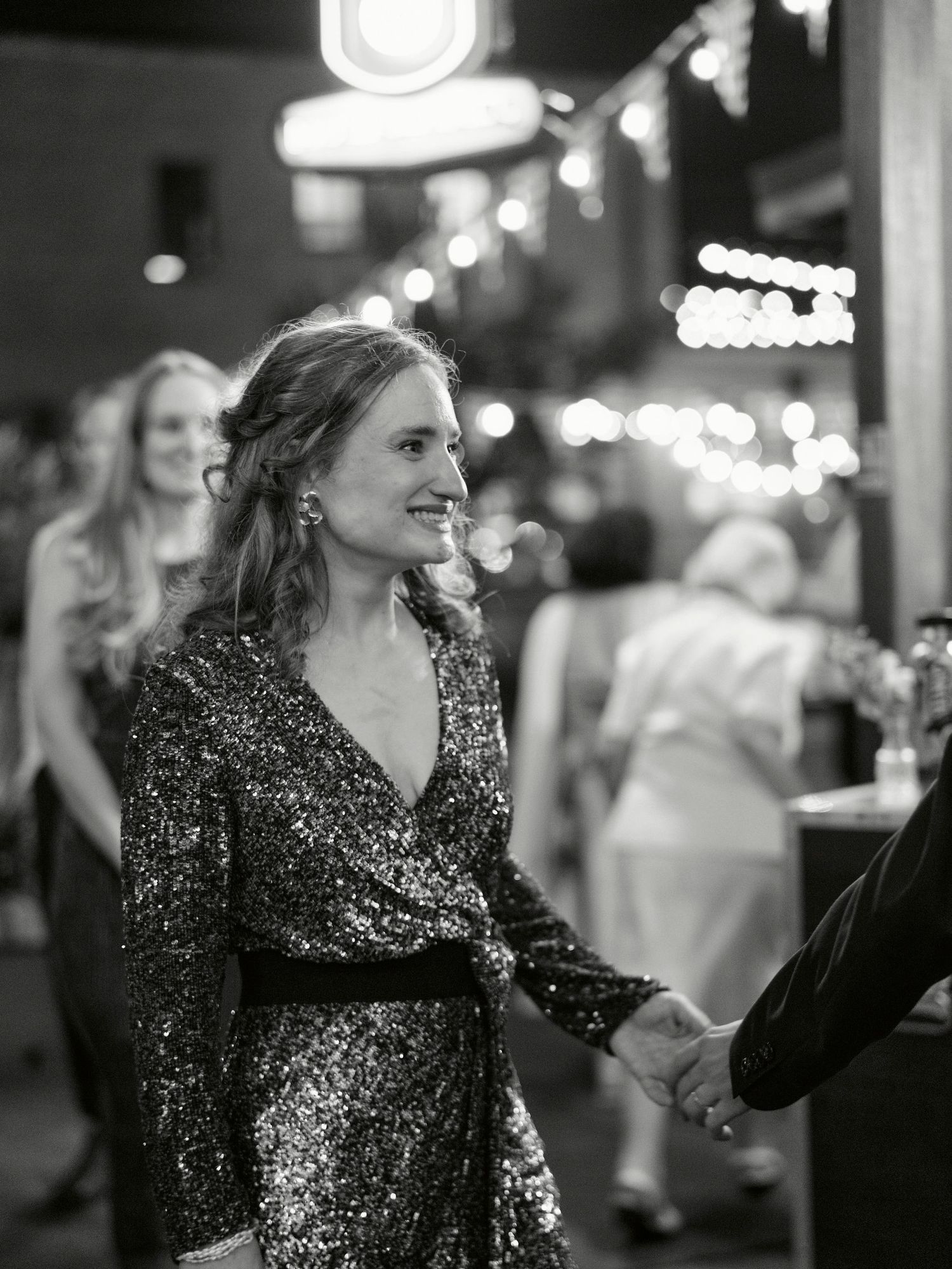 Woman in a sequined wrap dress stands in a dimly lit venue with string lights in the background.