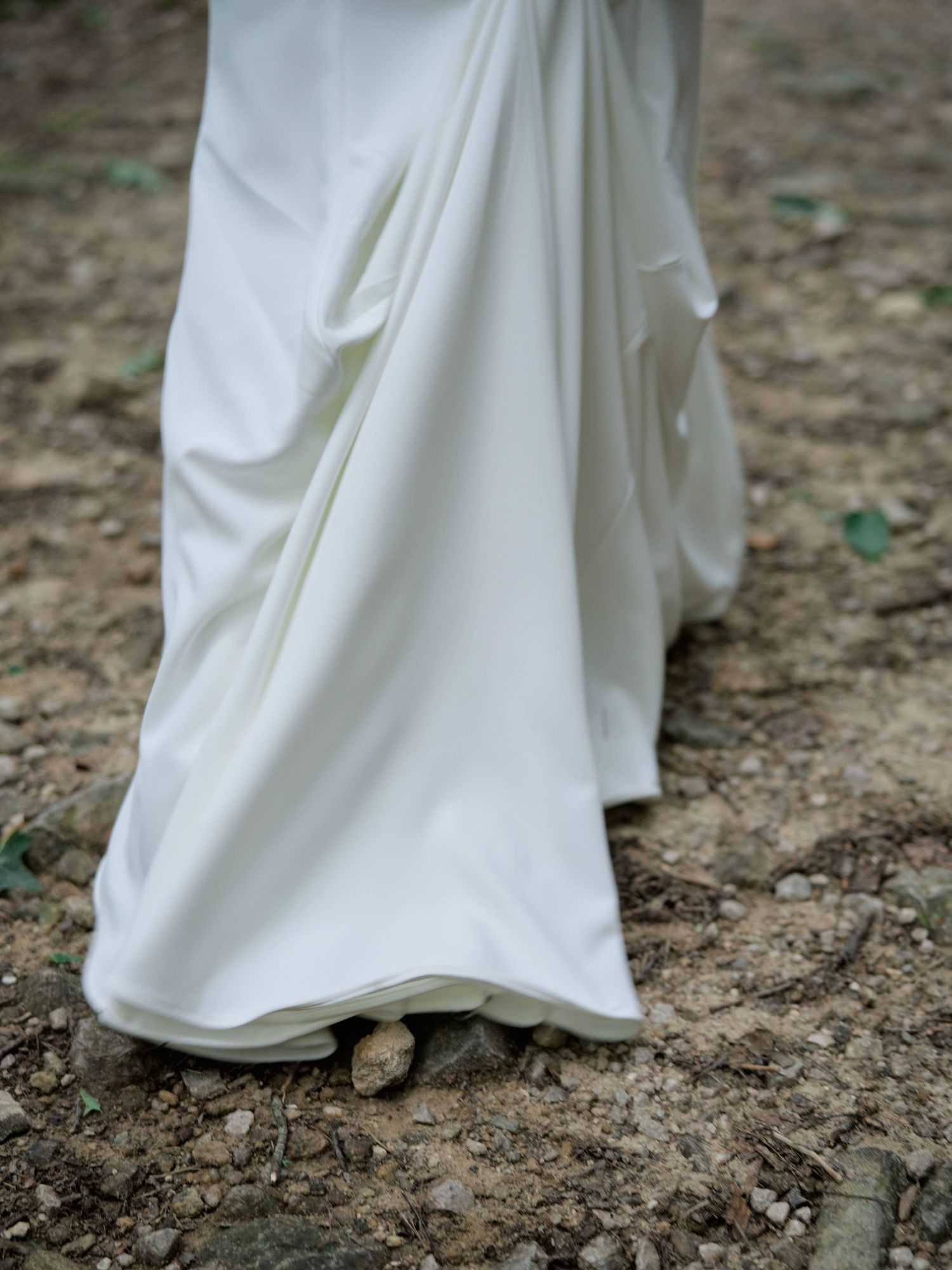 The hem of a flowing white wedding dress trails elegantly across rough ground in a series of artistic detail shots.