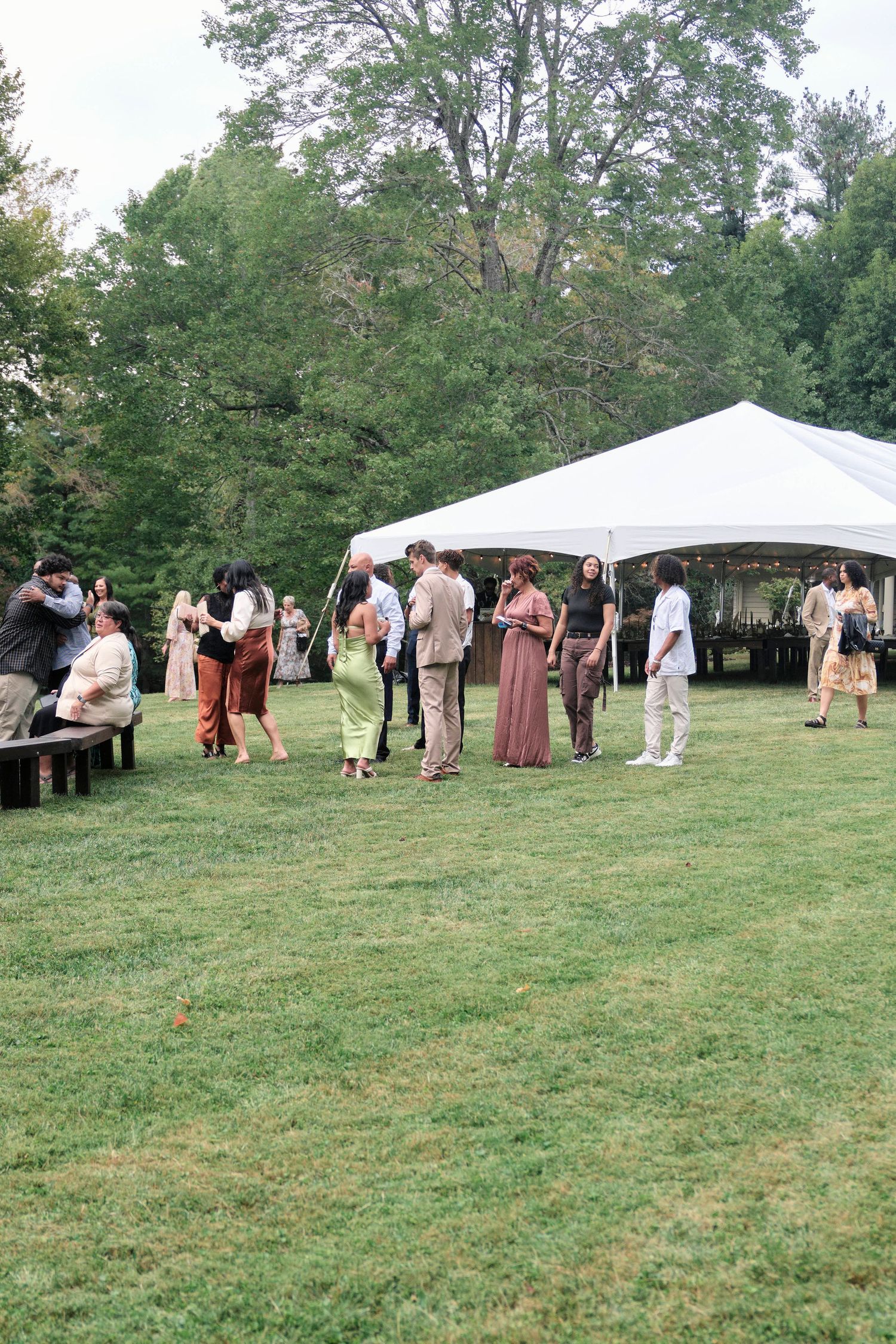 Wedding guests gather under a white tent during an outdoor reception.