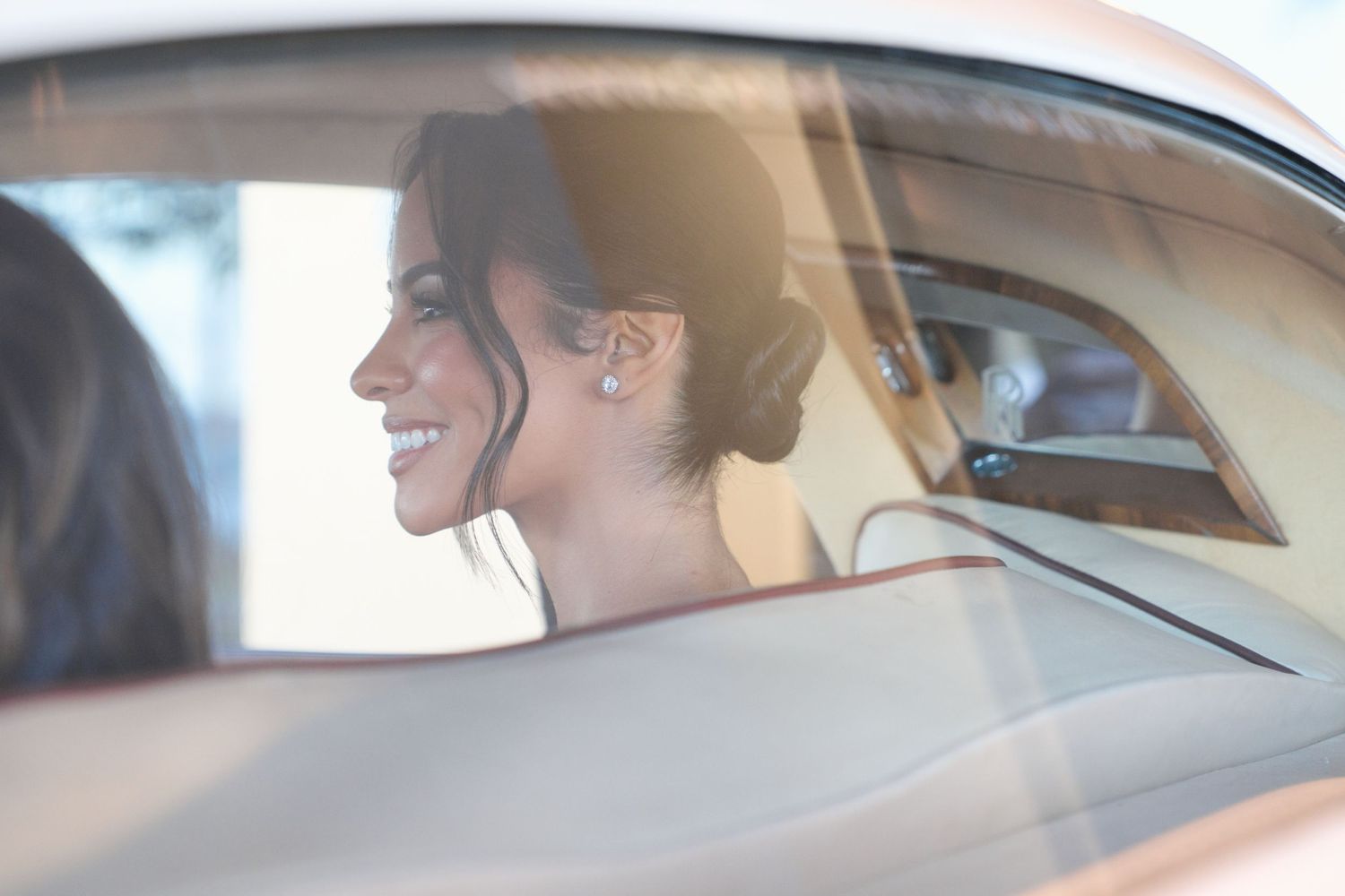 Happy bride seen through car window with elegant updo hairstyle.