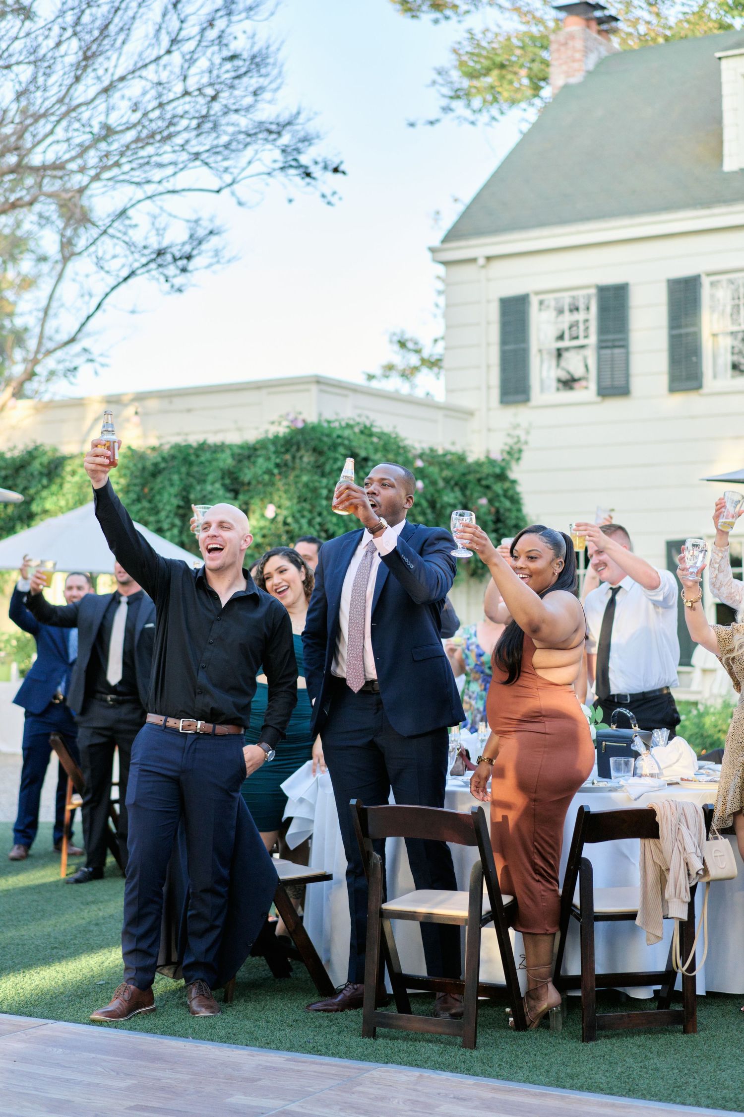 Wedding guests raise their glasses in celebration during an outdoor reception.