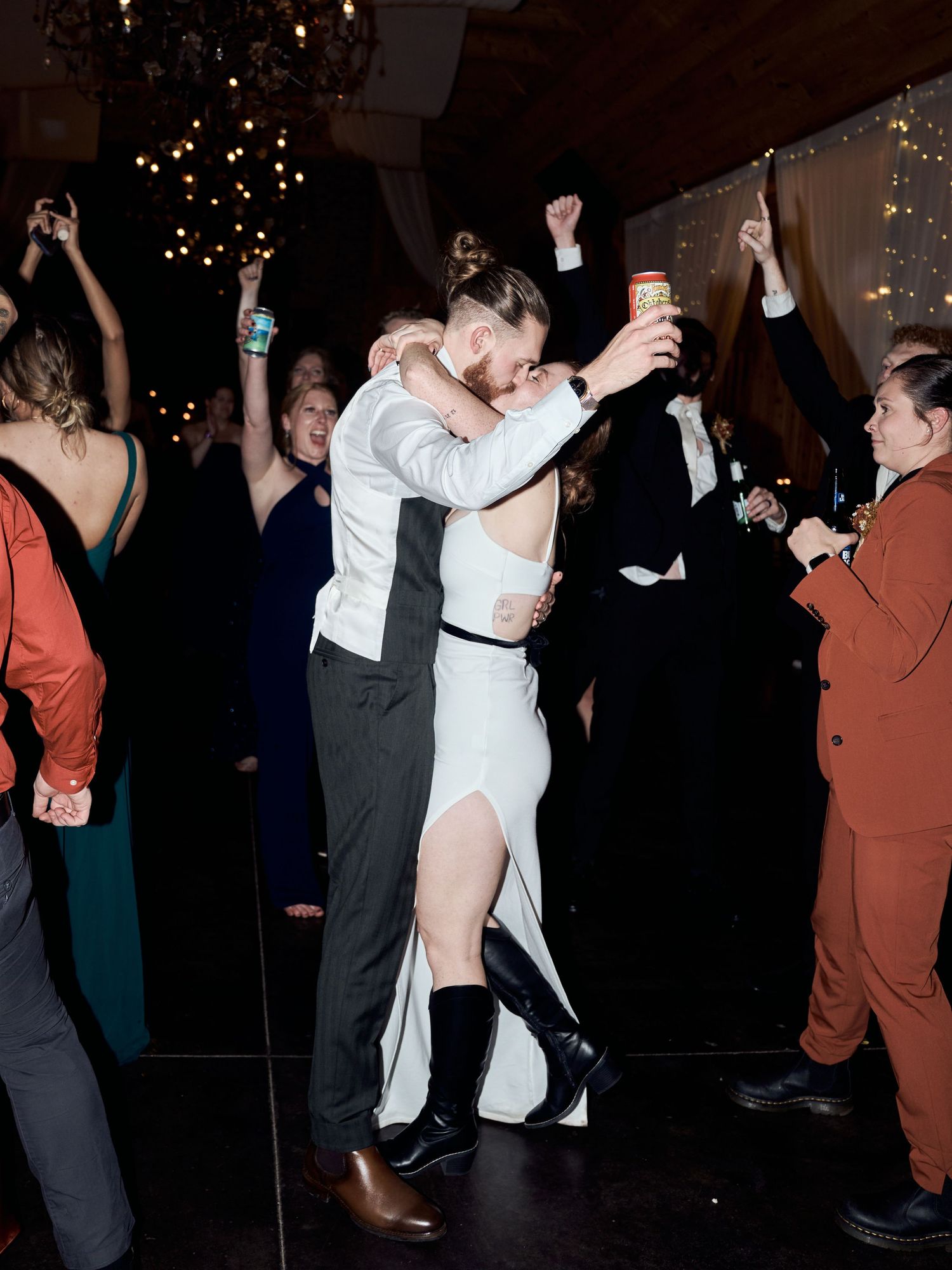 Wedding guests dance and celebrate on the dance floor under glowing chandeliers.