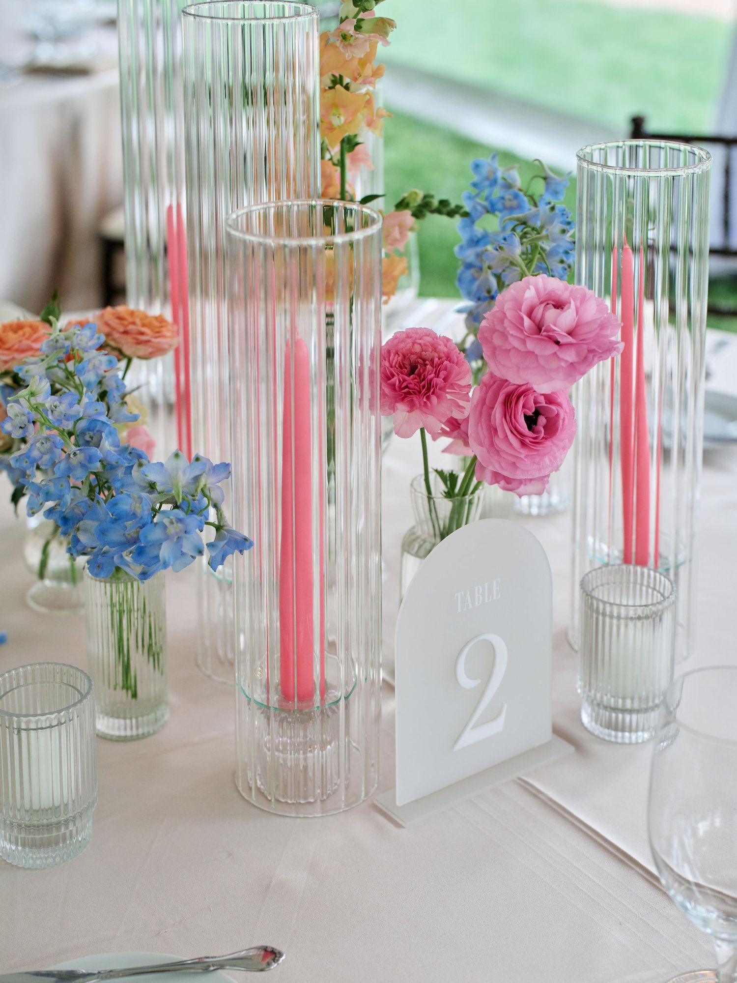 Glass vases with pink ranunculus and blue delphinium flowers create an elegant table centerpiece arrangement.