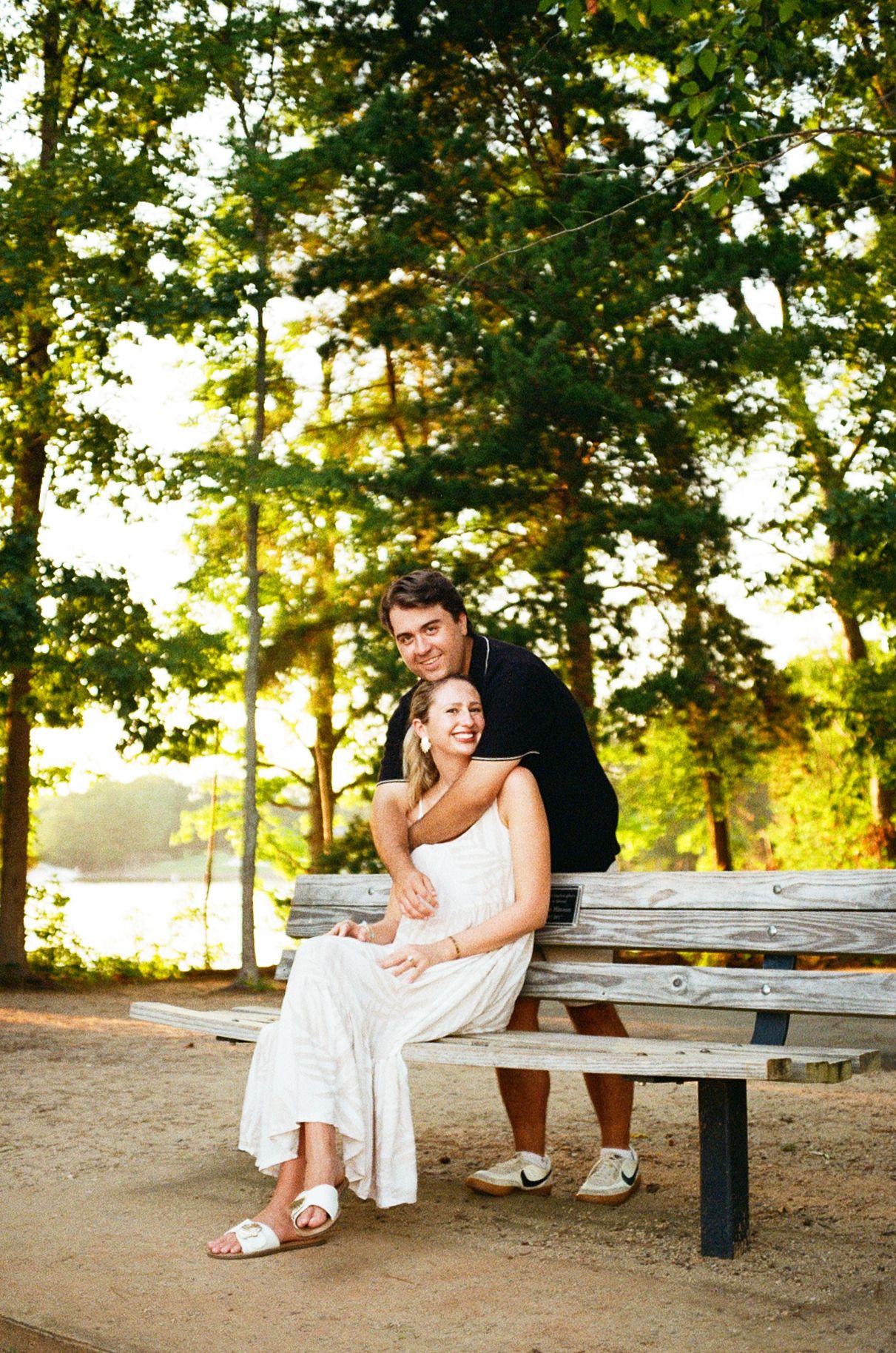 A romantic couple shares playful moments on a park bench during a sunny afternoon photo session.