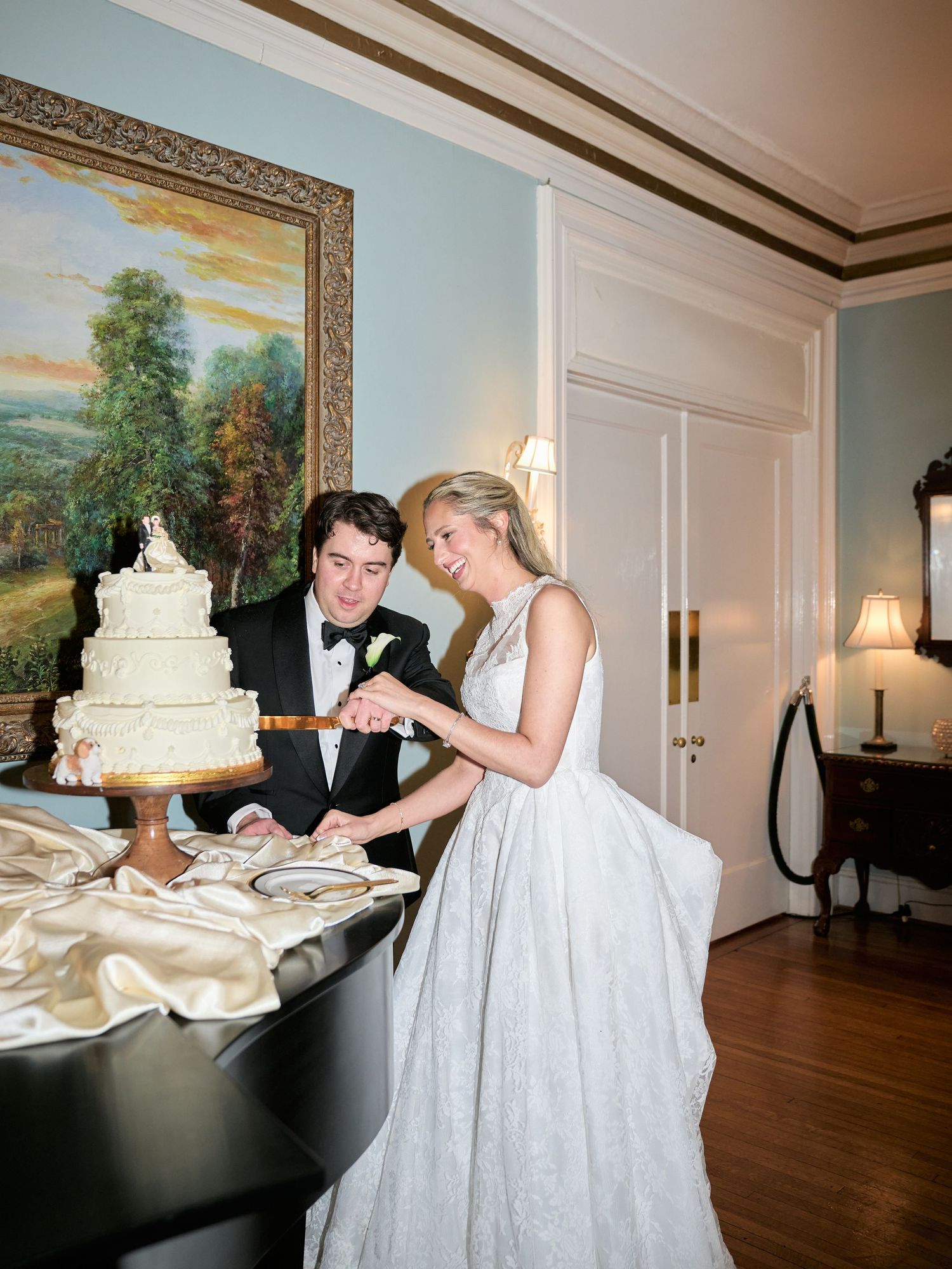 Bride and groom cutting their white wedding cake together in an elegant room with classic decor.