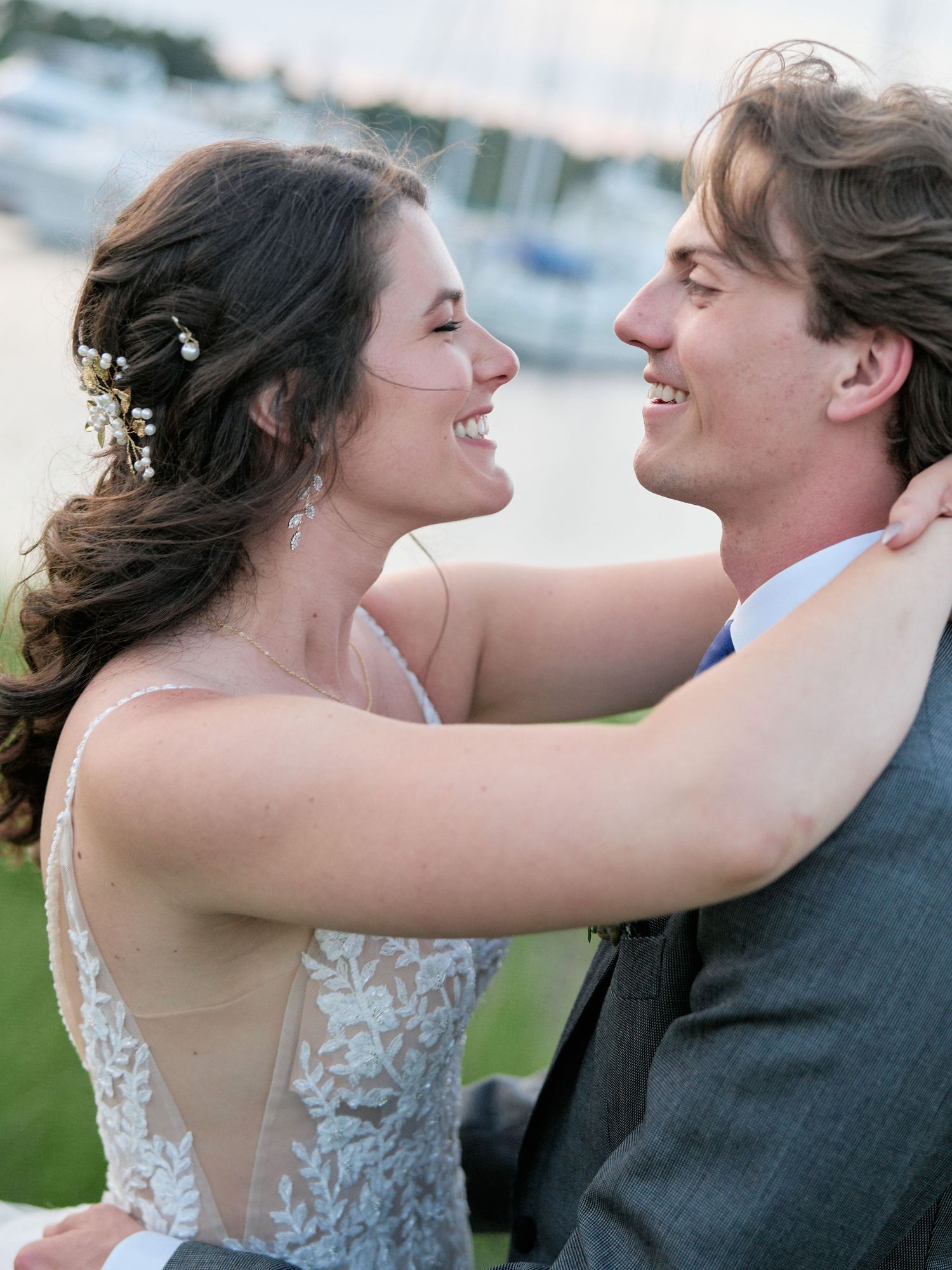 A joyful couple embraces and shares a laugh during their wedding photoshoot by a marina at sunset.