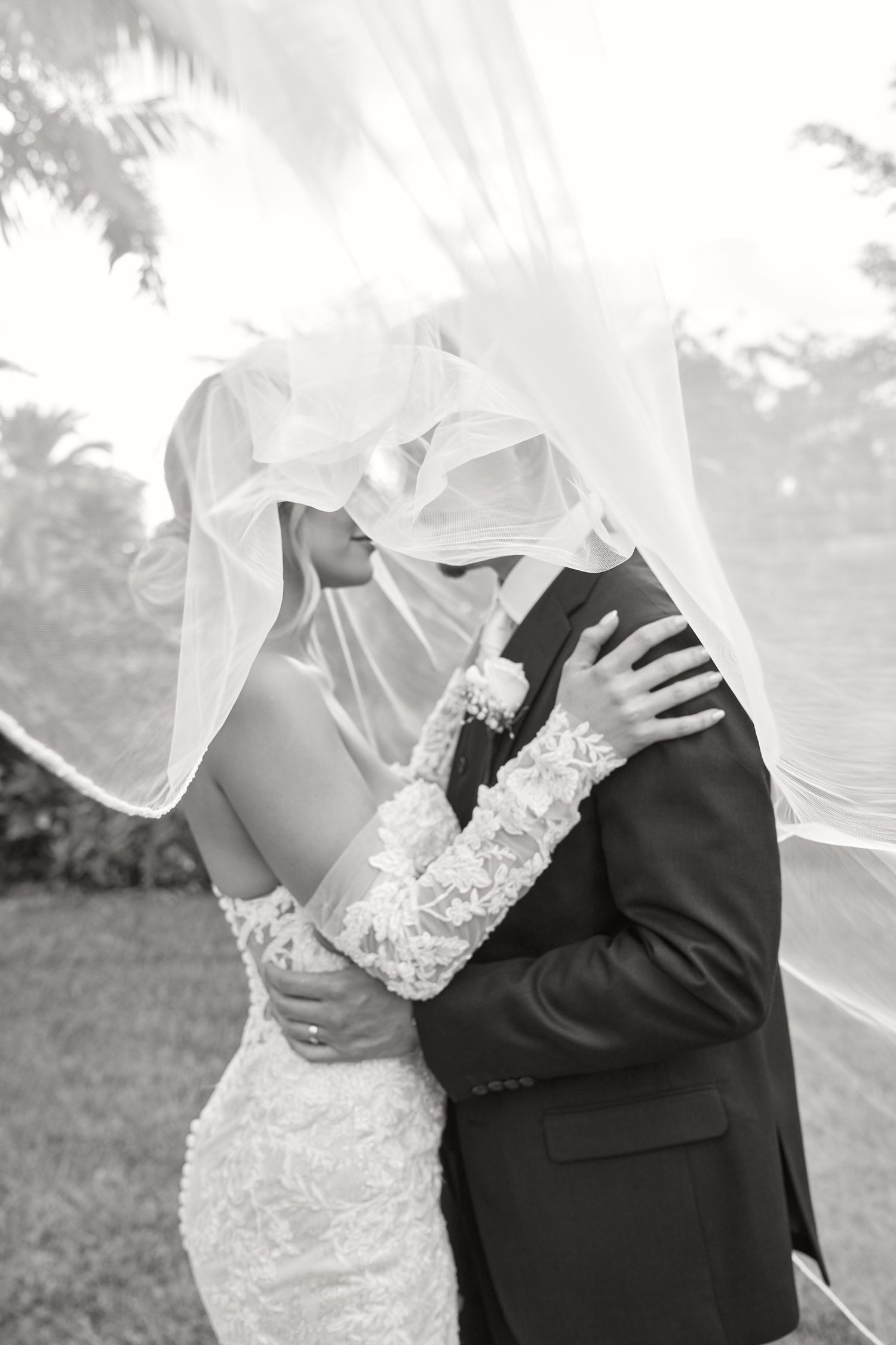 Romantic black and white portrait of couple beneath flowing wedding veil.
