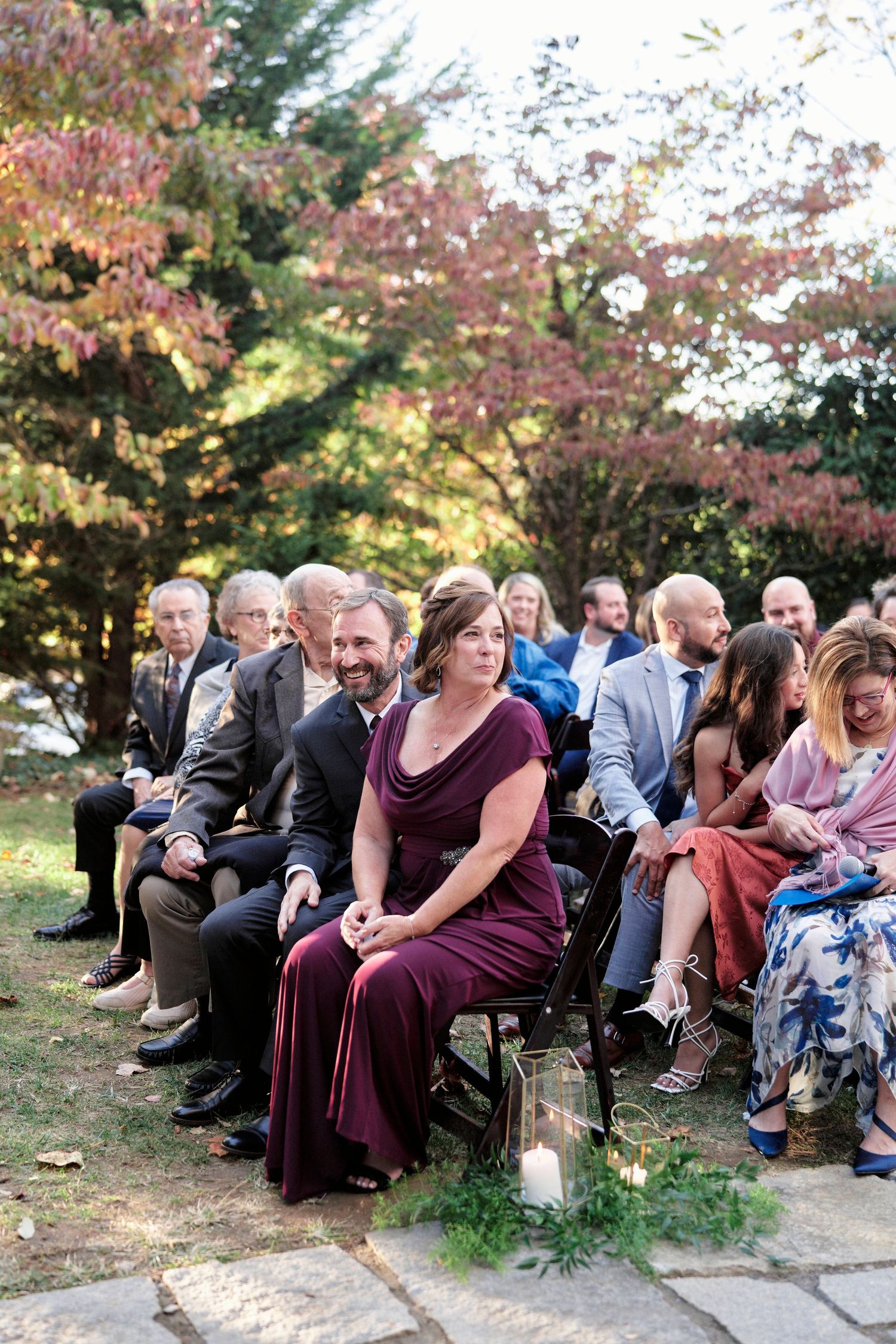 Wedding guests seated in burgundy and formal attire during outdoor autumn ceremony.